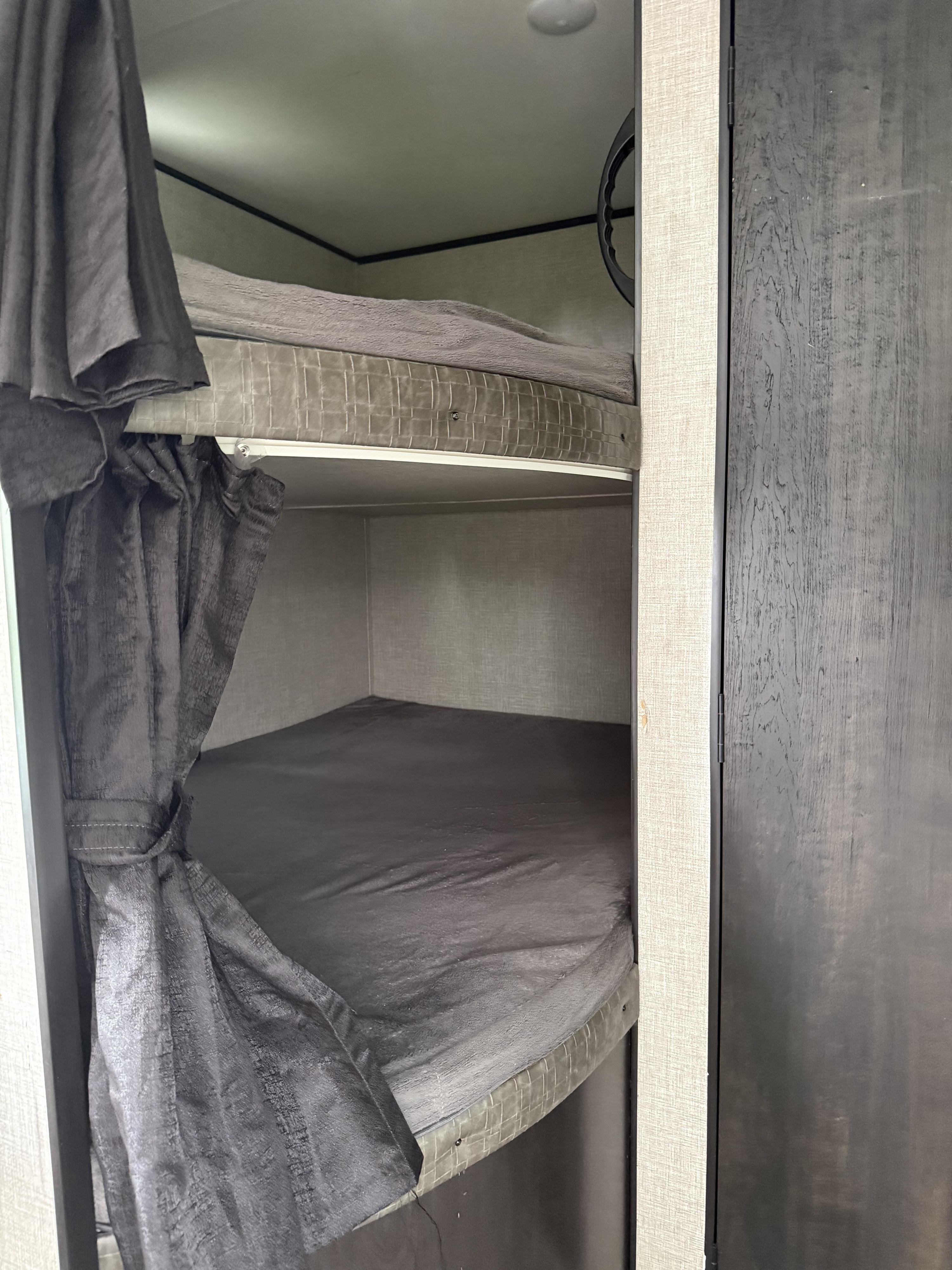 Bunk beds with privacy curtains and dark bedding in an RV rental, offering comfortable sleeping for travel.. Jayco Jay Flight SLX 2022