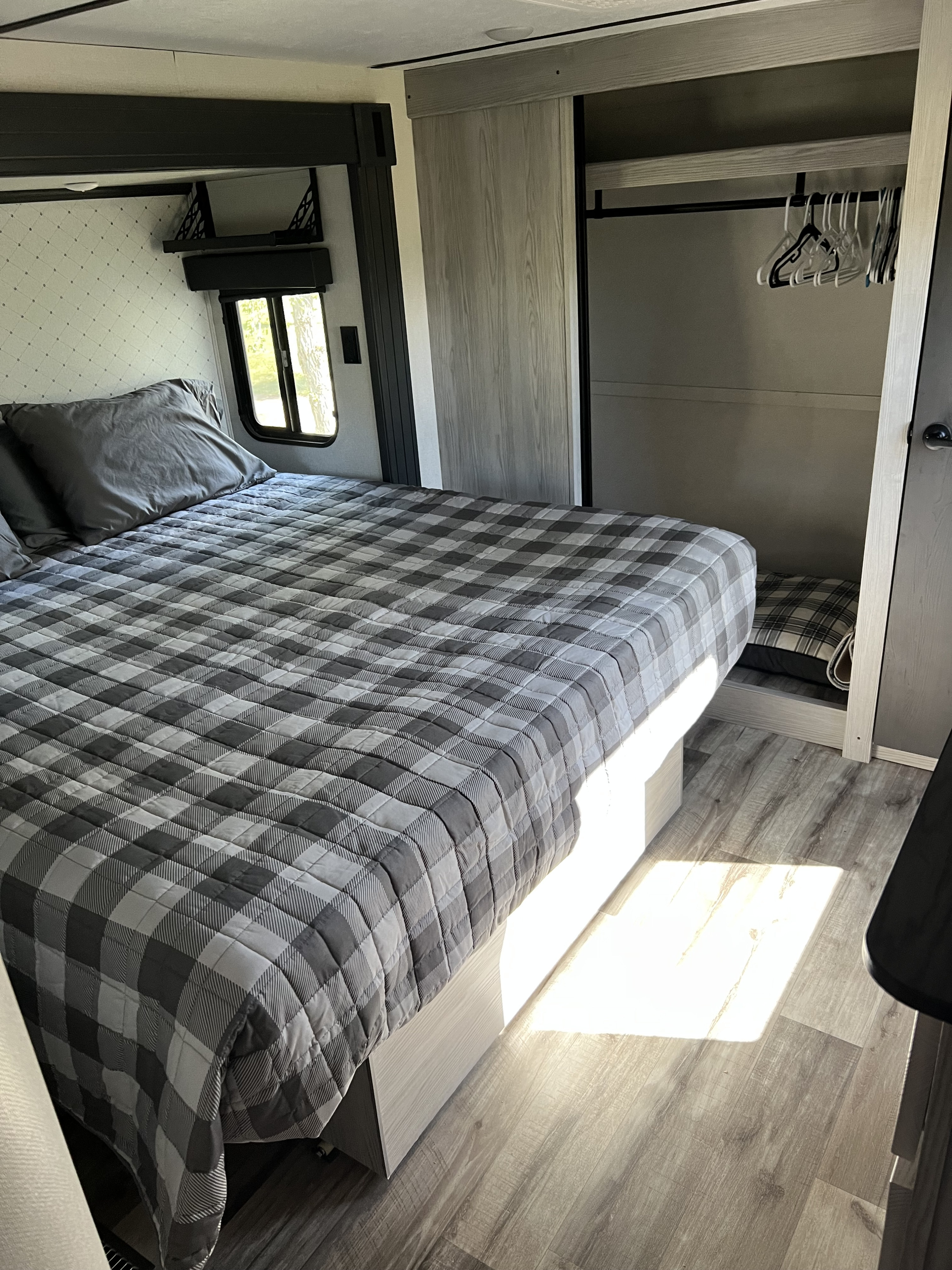 Inviting rv rental bedroom with a comfy plaid bed, window, spacious closet, and sunny wood-look floor.. Keystone RV Montana 2022