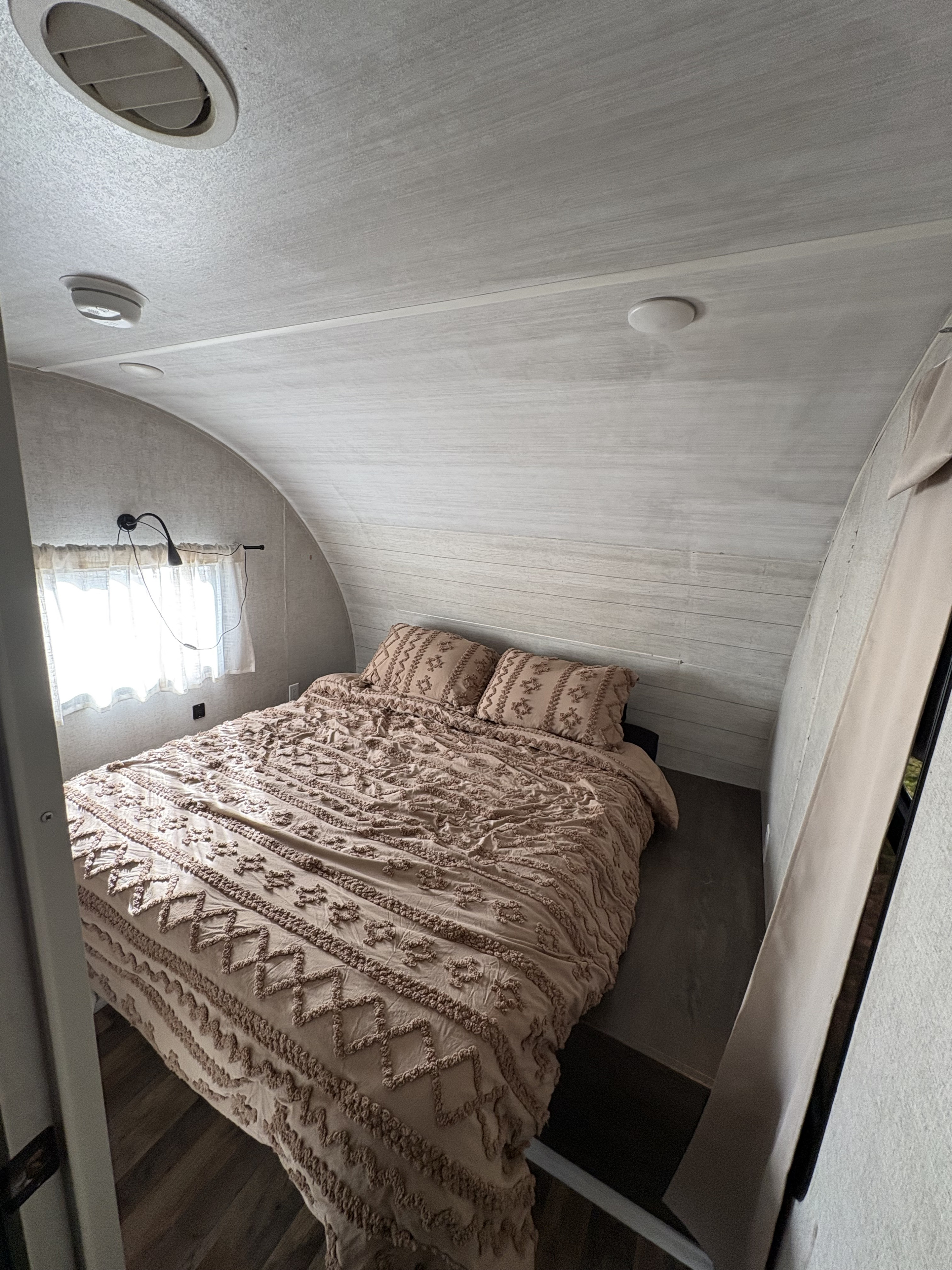 Cozy RV rental bedroom featuring a full bed with textured bedding, window light, and curved ceiling.. Forest River Salem Cruise Lite 2020