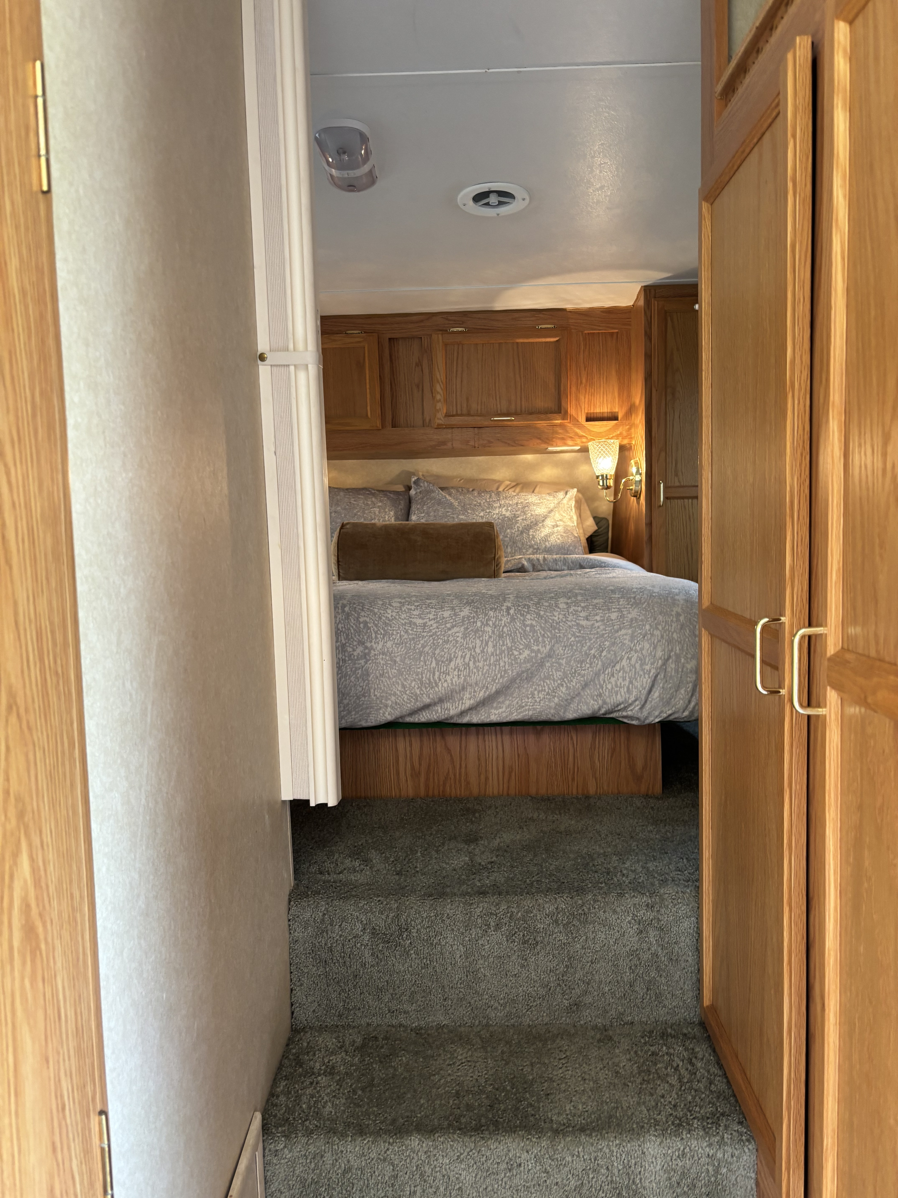 Cozy RV rental bedroom with carpeted steps, a comfortable bed, and warm wood cabinetry.. Jayco Qwest 2003