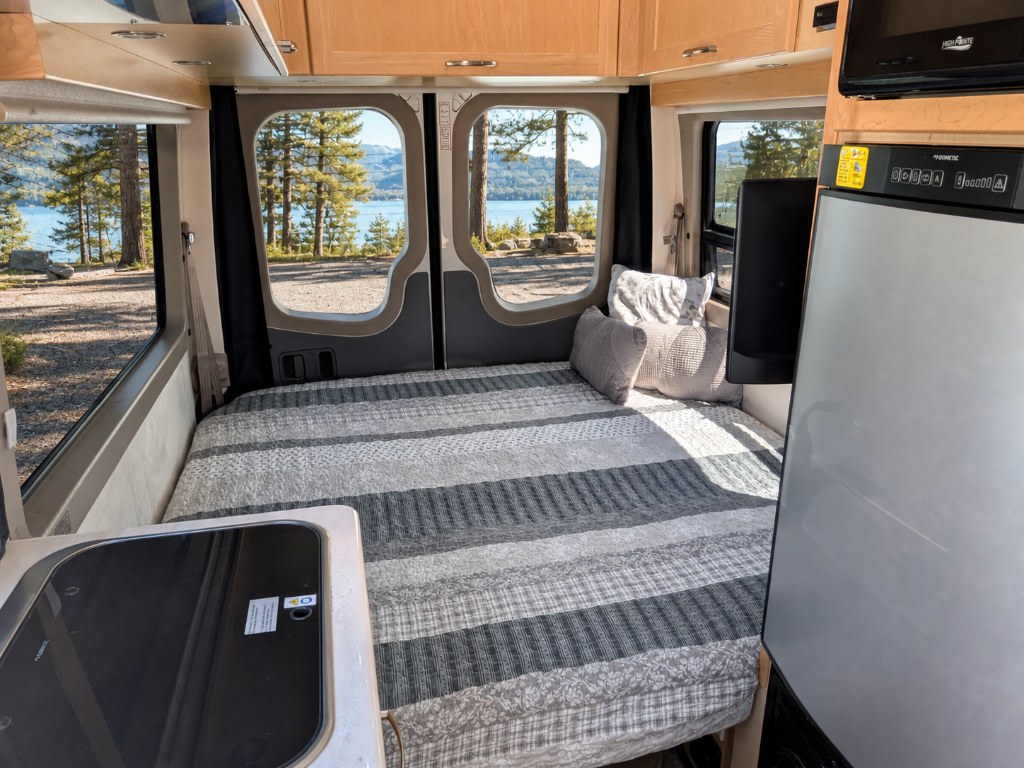 RV rental interior: striped bed, compact kitchen with stovetop, refrigerator, and scenic lake & forest view.. Pleasure-Way Pleasure-Way Class B 2016