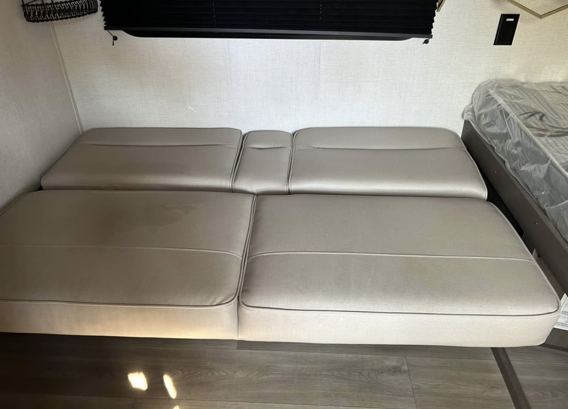Convertible sofa bed in an RV rental interior, showing a stain on the cushion. Ideal for flexible sleeping arrangements.. Grand Design Transcend One 2025