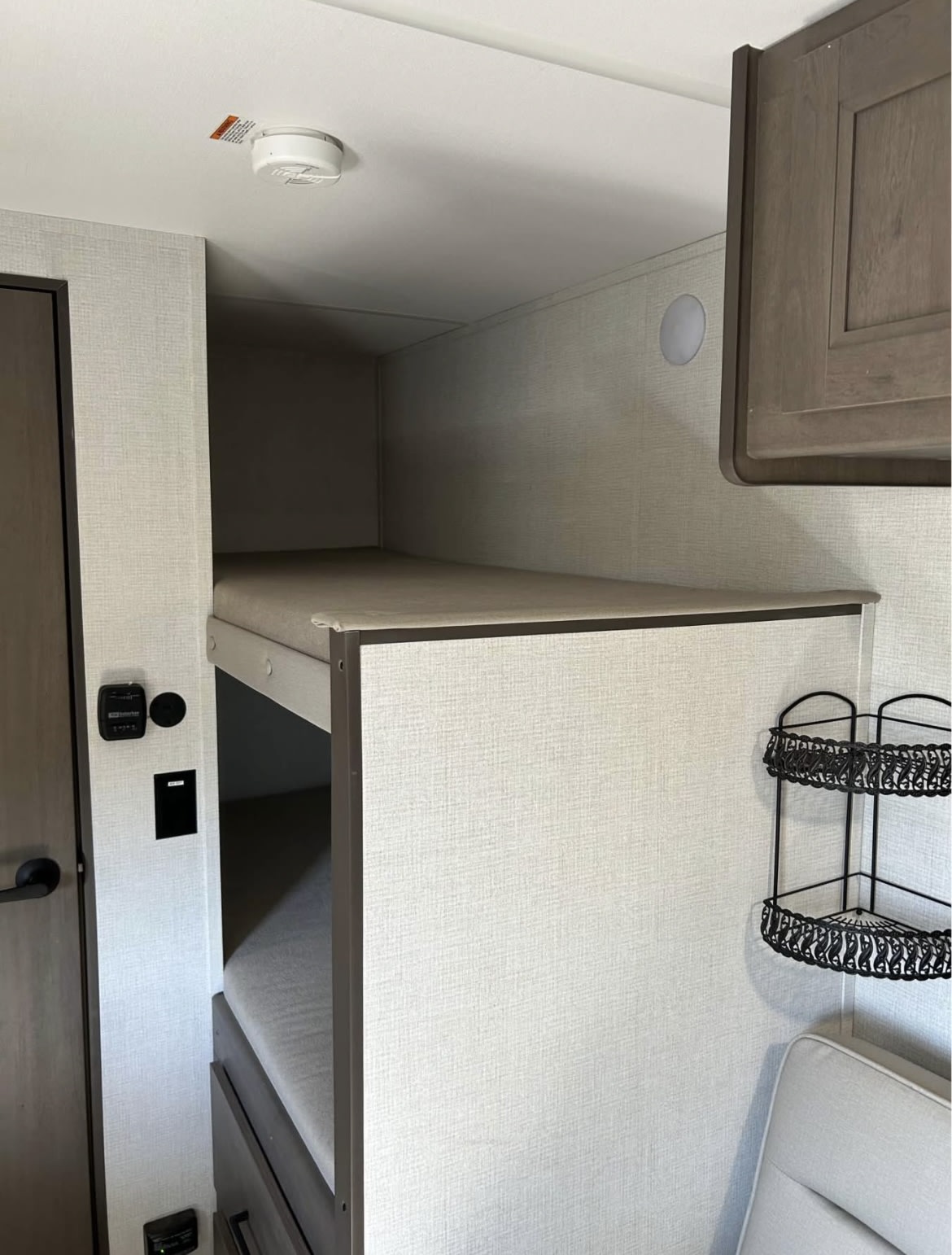 Interior of an rv rental showing bunk beds, a smoke detector, wall controls, and corner storage shelves, optimized for compact living.. Grand Design Transcend One 2025