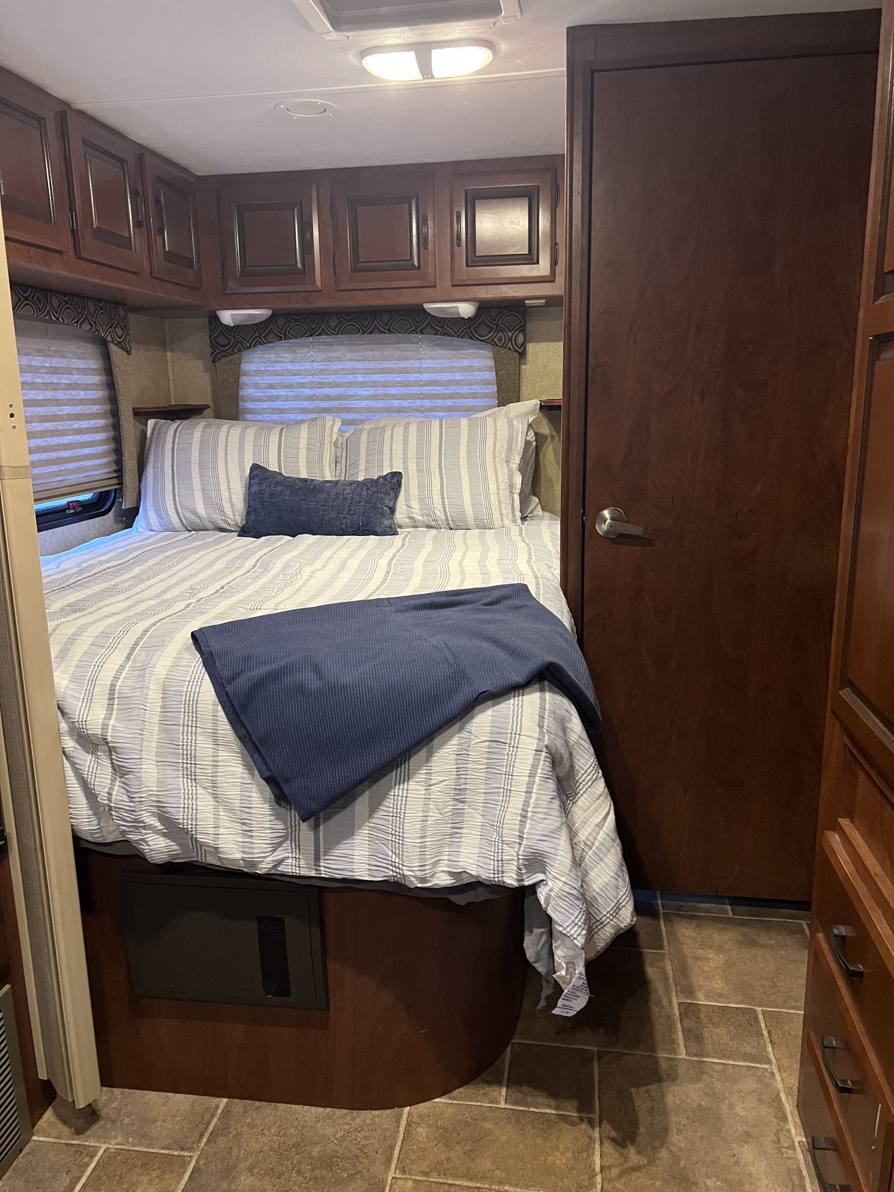 Cozy RV rental bedroom featuring striped bedding, a blue throw, dark wood cabinets, and a compact design.. Forest River Sunseeker 2013