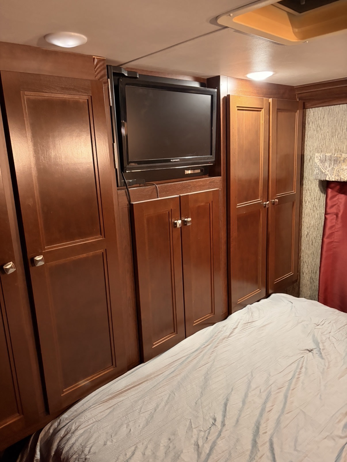 RV rental interior: a bedroom with dark wood cabinets, a mounted TV, and a light-colored bed, maximizing space.. Forester 3051s 2018