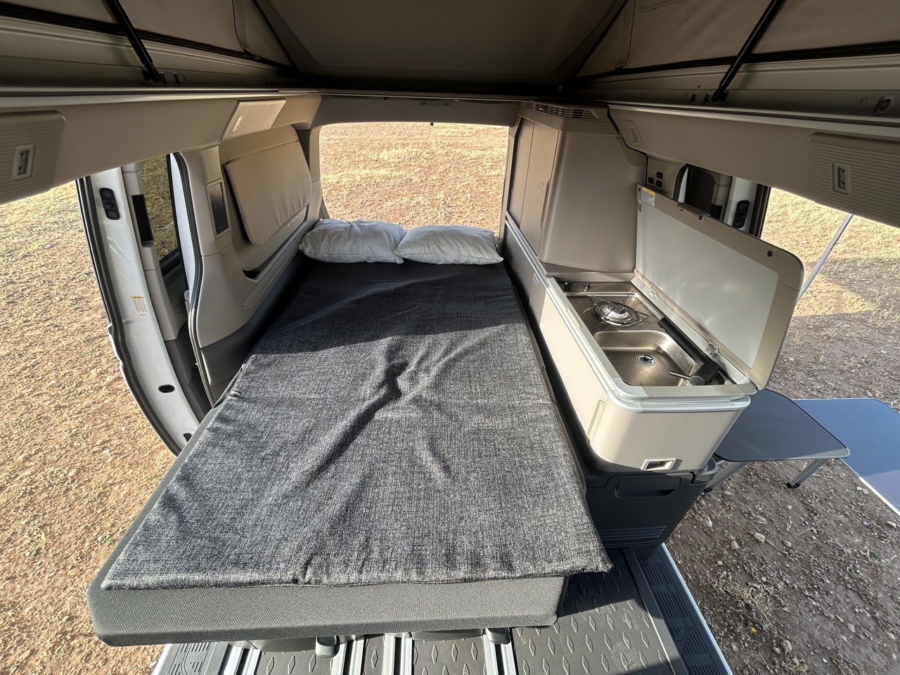 View inside an rv rental campervan, featuring a comfy bed, a compact kitchen with stove and sink, and a table.. Volkswagen California Ocean 2026