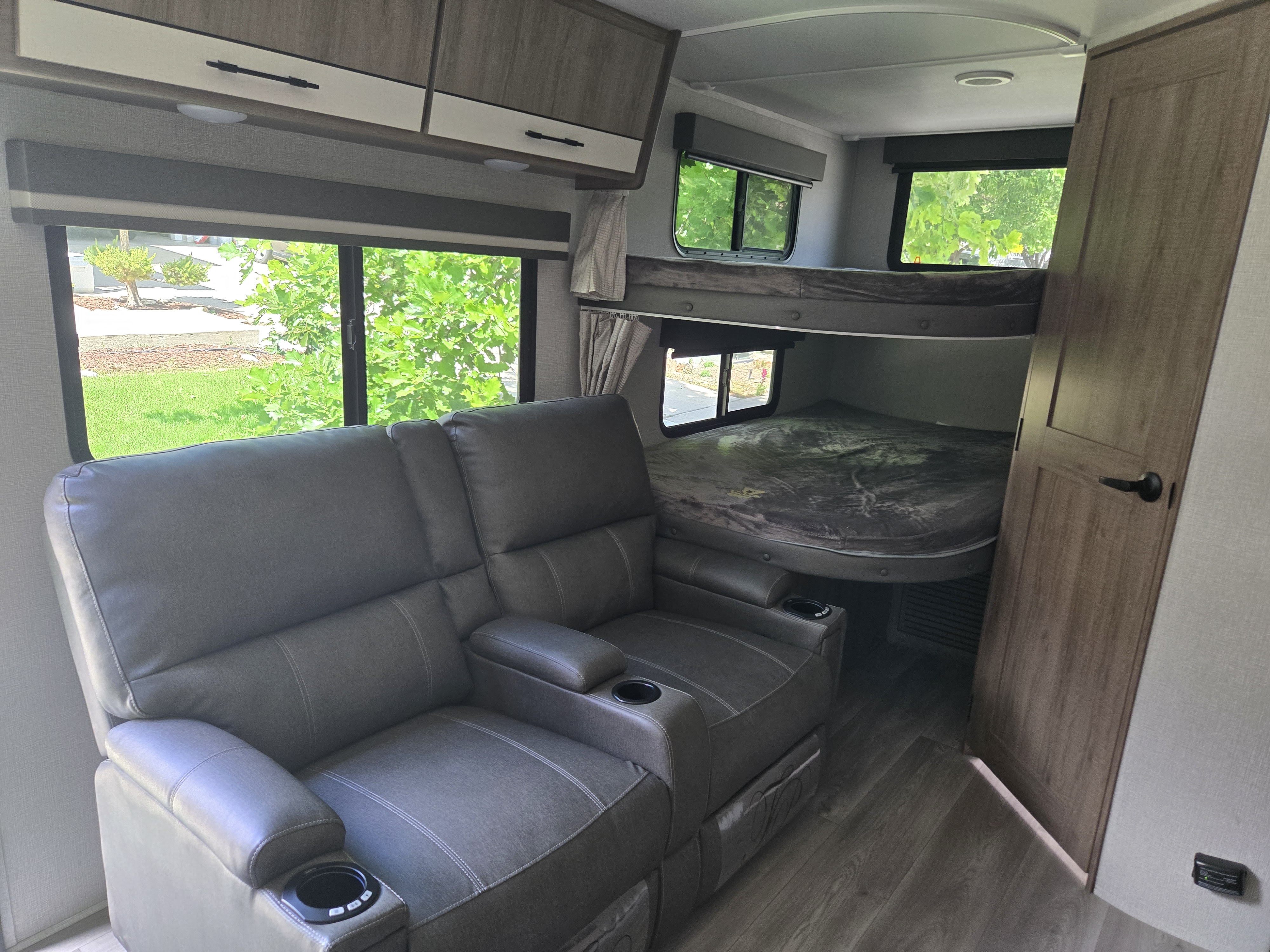 Cozy RV rental interior featuring comfy gray recliners, bunk beds, and large windows, perfect for family travel.. Grand Design Imagine XLS 2024
