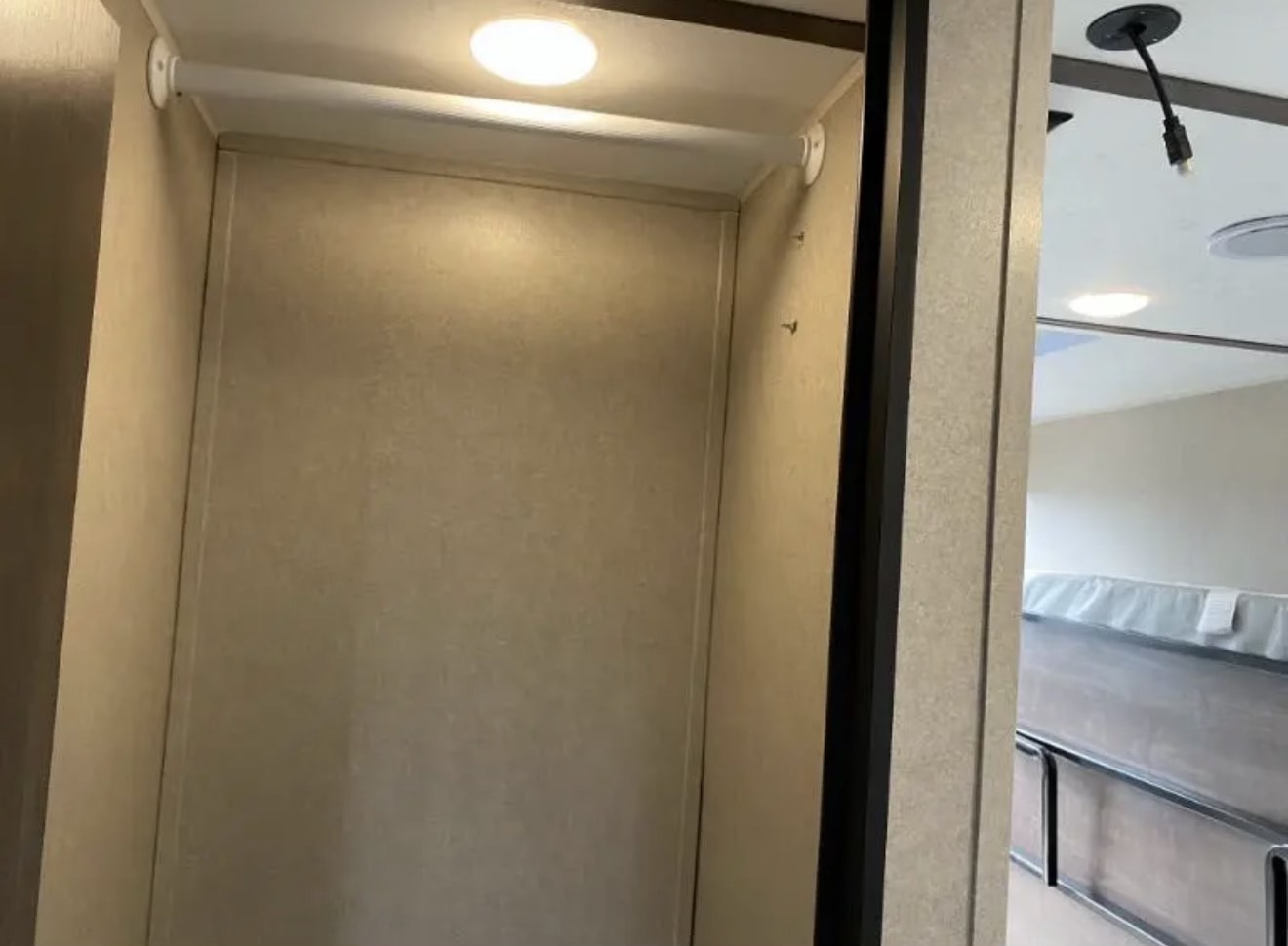 Inside an RV rental: a lit closet/storage space with hooks, next to bunk beds in the sleeping area.. Sunset Park RV SunRay 2022