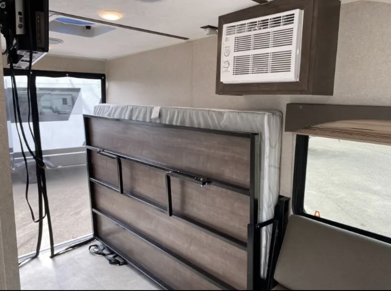 RV rental: Interior of a toy hauler camper with a folded bed, wall-mounted AC unit, and view through the rear ramp door.. Sunset Park RV SunRay 2022