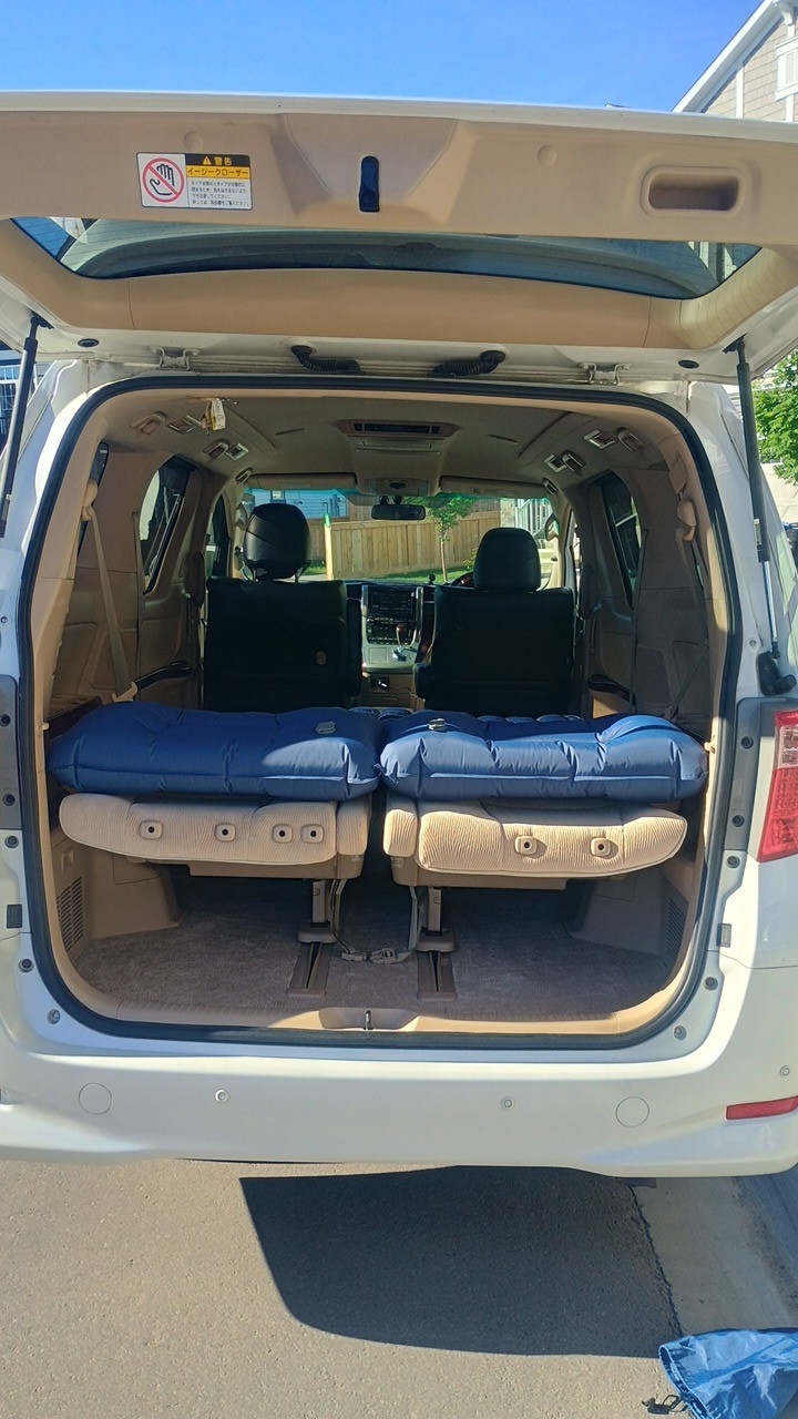 White RV rental minivan, tailgate open, reveals two blue sleeping pads on beige folded rear seats, ready for car camping.. Toyota Hiace 2009