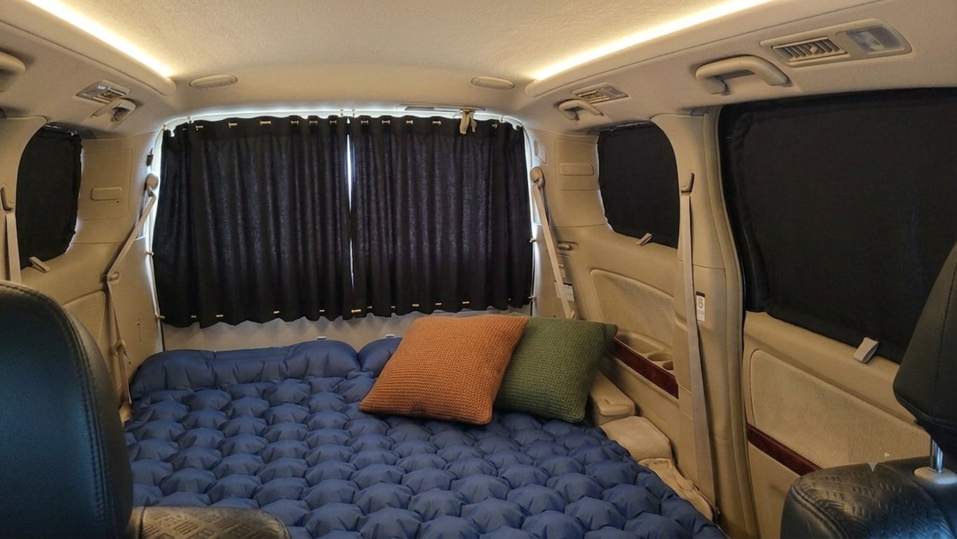 Cozy RV rental interior with an inflatable bed, pillows, and blackout curtains for private camping and travel.. Toyota Hiace 2009