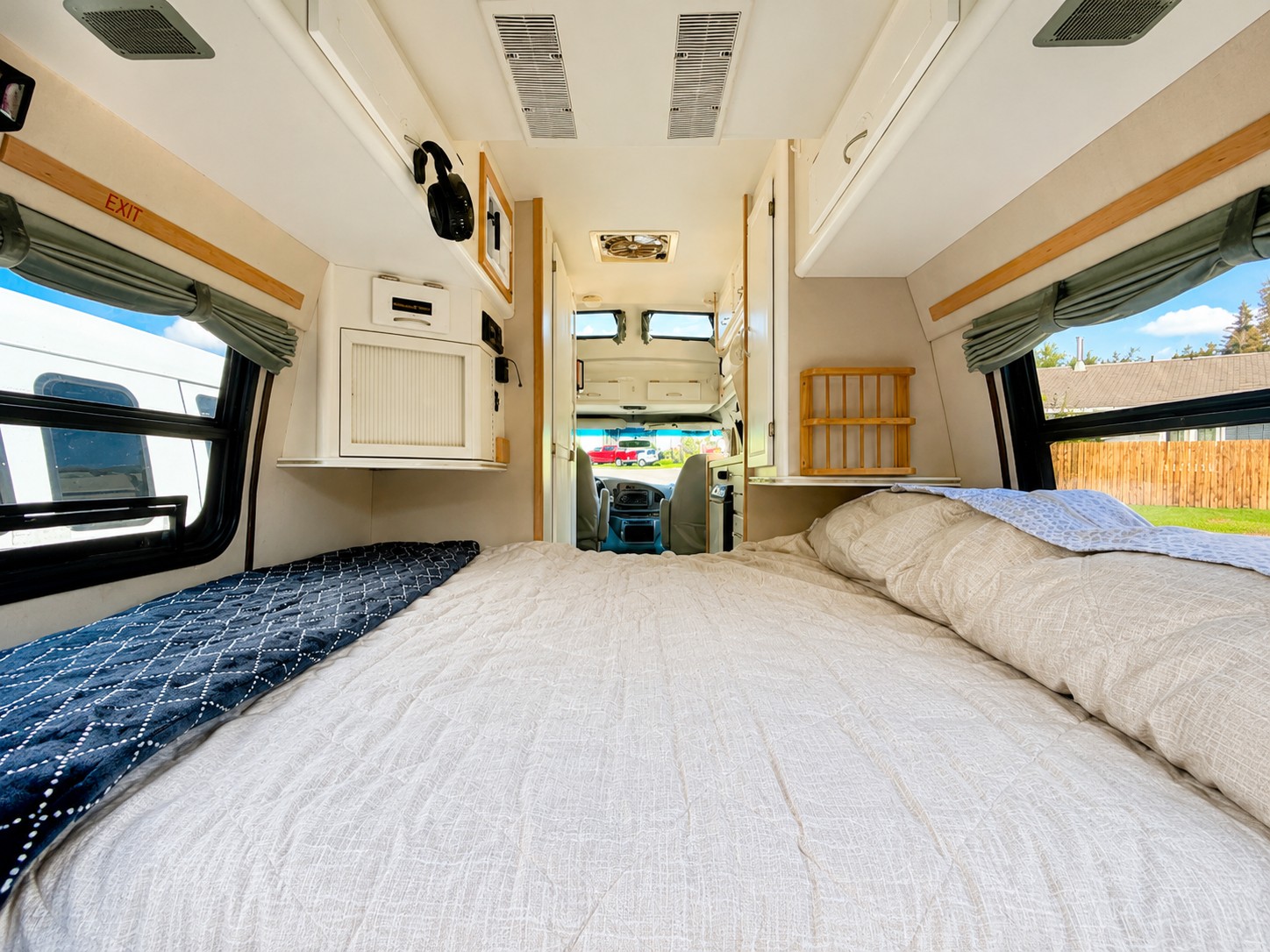 Spacious RV rental bedroom featuring a large, inviting bed, overhead storage, and bright windows with outdoor views.. Pleasure-Way Excel TS 2002