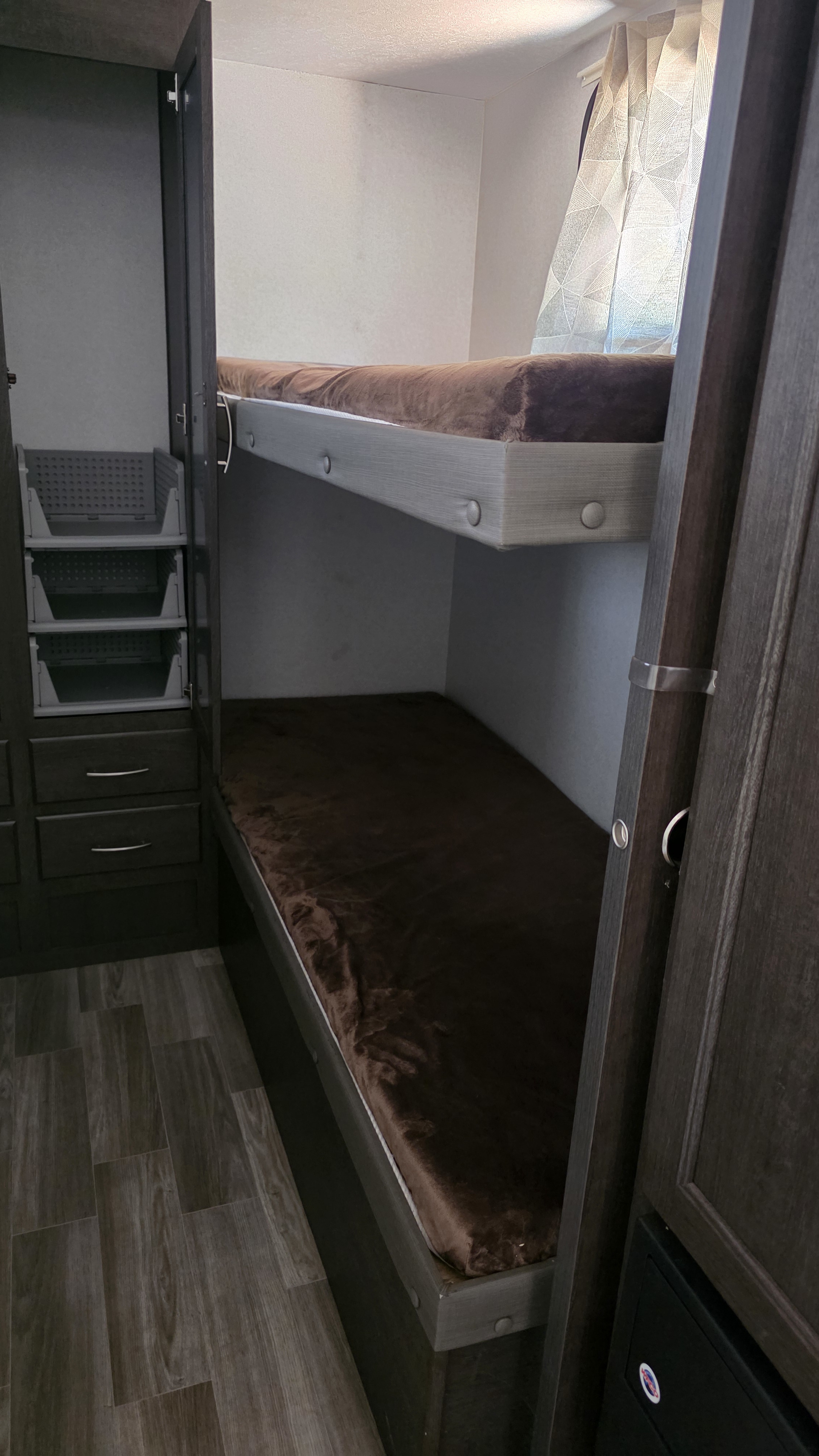 Cozy RV rental bunk beds with soft brown covers & integrated storage. Perfect for a compact camper interior.. Forest River Wildwood X-Lite 2019