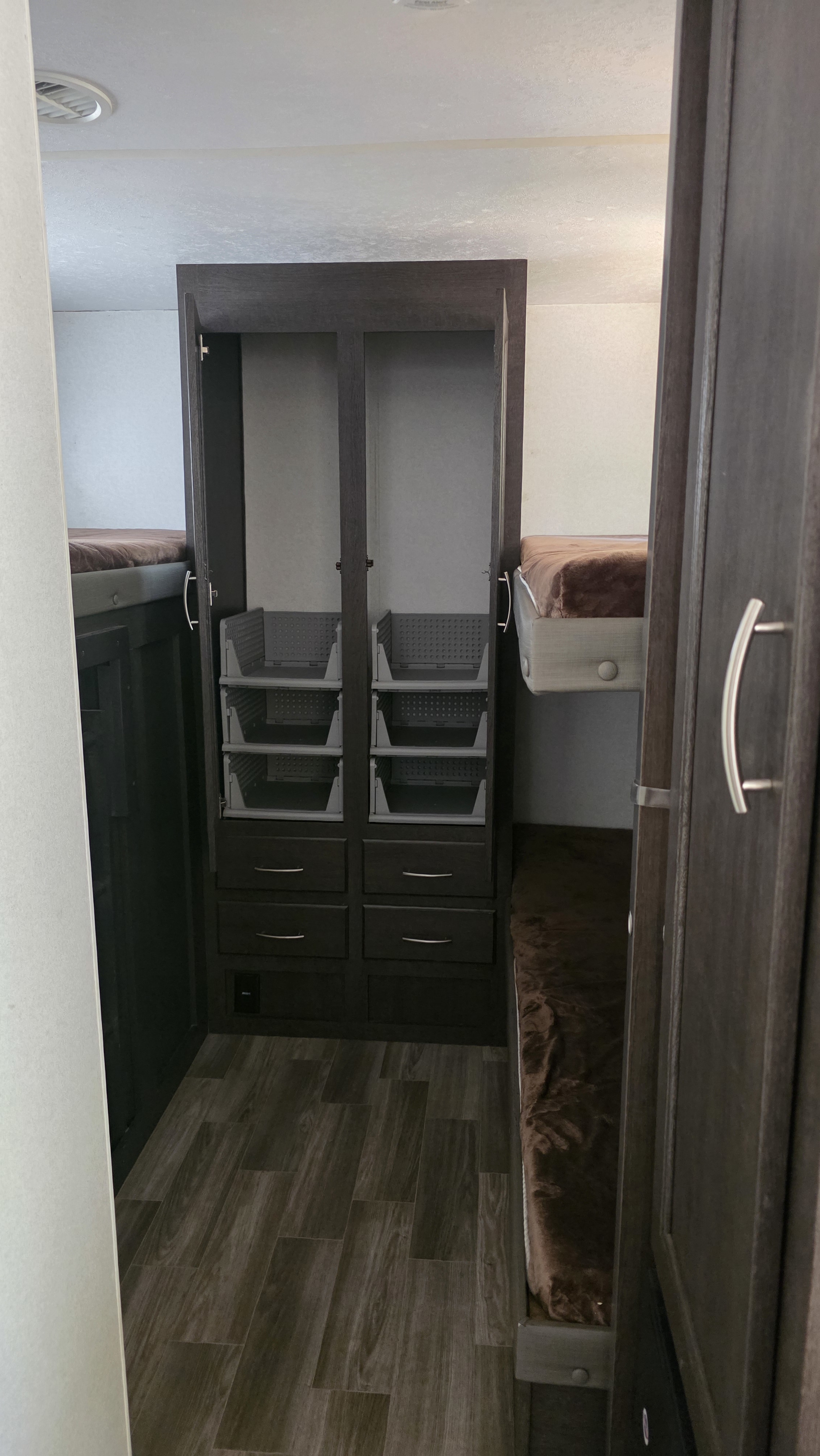 RV rental bunkhouse interior with dark wood storage unit, open doors showing grey bins, bunk beds, and wood-look floor.. Forest River Wildwood X-Lite 2019