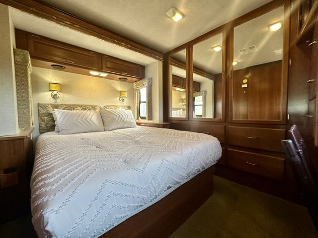 Cozy RV rental bedroom featuring a comfortable bed, overhead cabinets, and mirrored closet doors. Ideal for your next adventure.. Fleetwood Southwind 2006