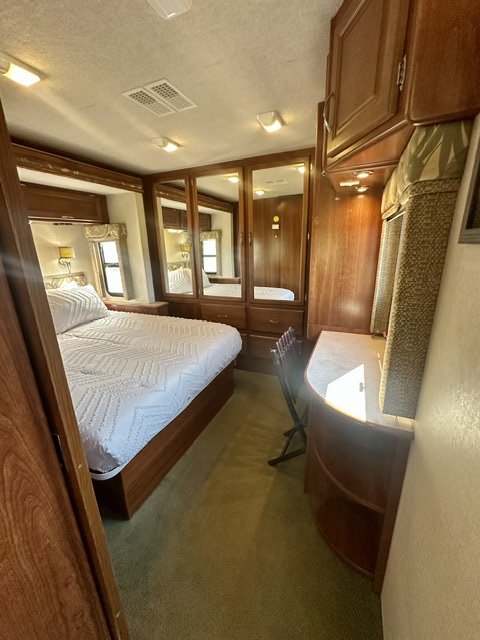 RV rental bedroom interior showing a bed, mirrored closet, and desk with wood cabinetry, carpeted floor.. Fleetwood Southwind 2006