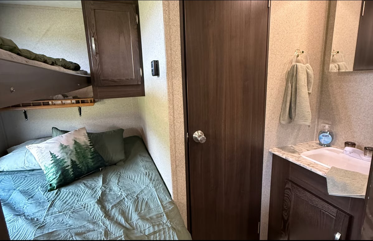 RV rental: cozy bedroom with bunk beds, forest-themed pillow, and an adjacent compact bathroom vanity with sink and towels.. Keystone RV Springdale 2019