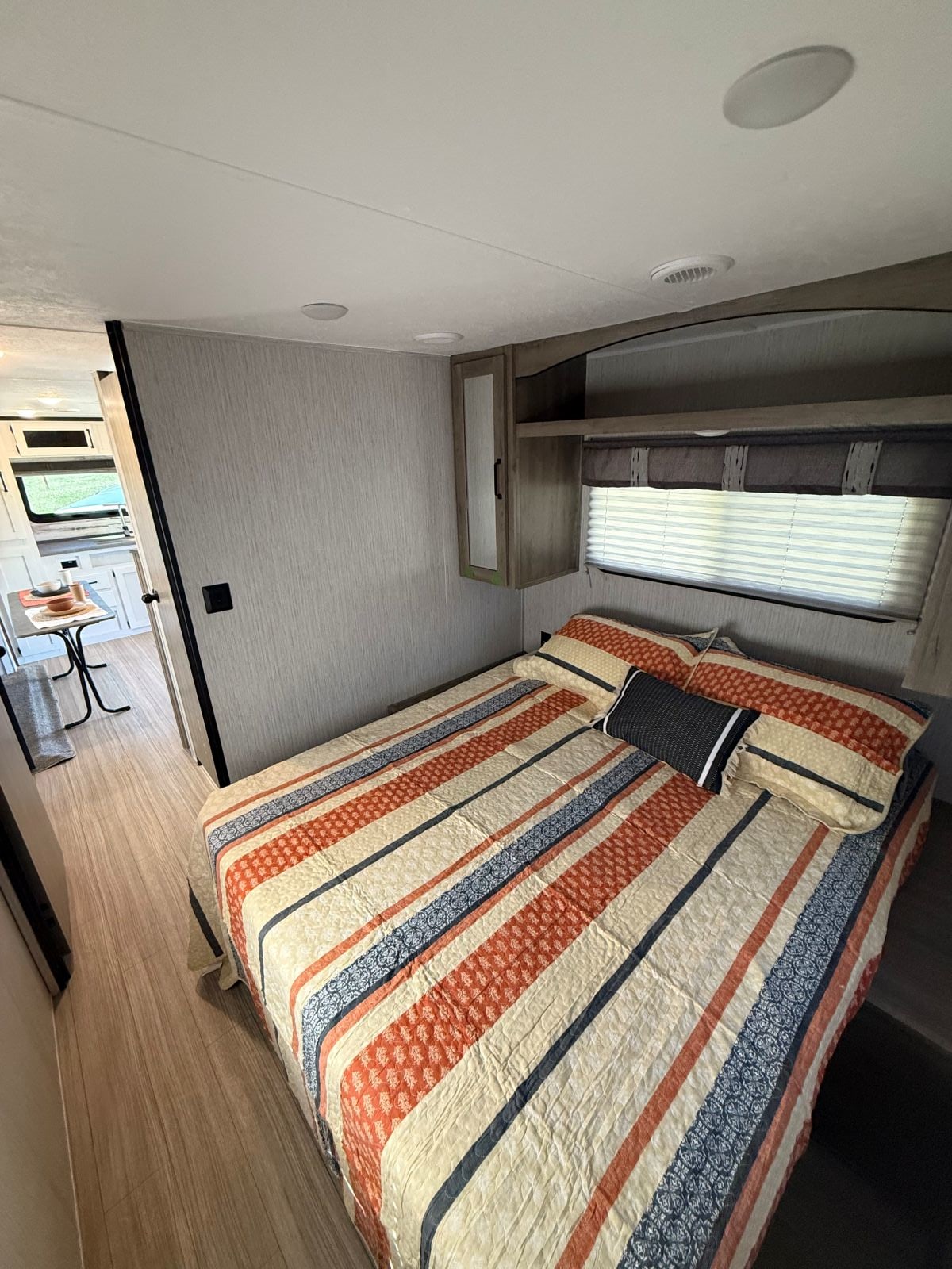 Inside a modern RV rental: a compact bedroom with a colorful striped bed, overhead cabinets, and a window with blinds.. Palomino Puma XLE Lite 2022