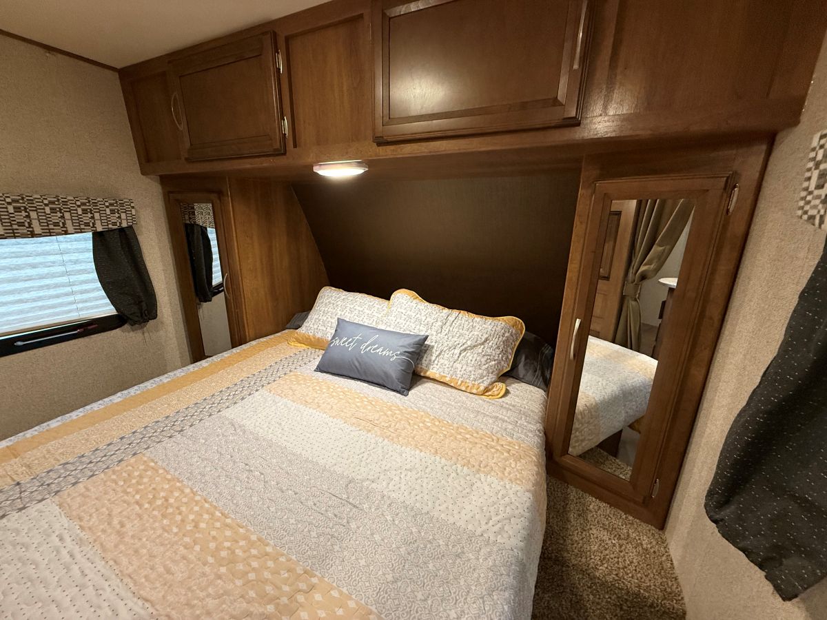 Cozy RV rental bedroom with patterned bedding, overhead cabinets, a window, and mirrored closets, creating a warm, inviting space.. Coachmen Apex Ultra Lite 2016
