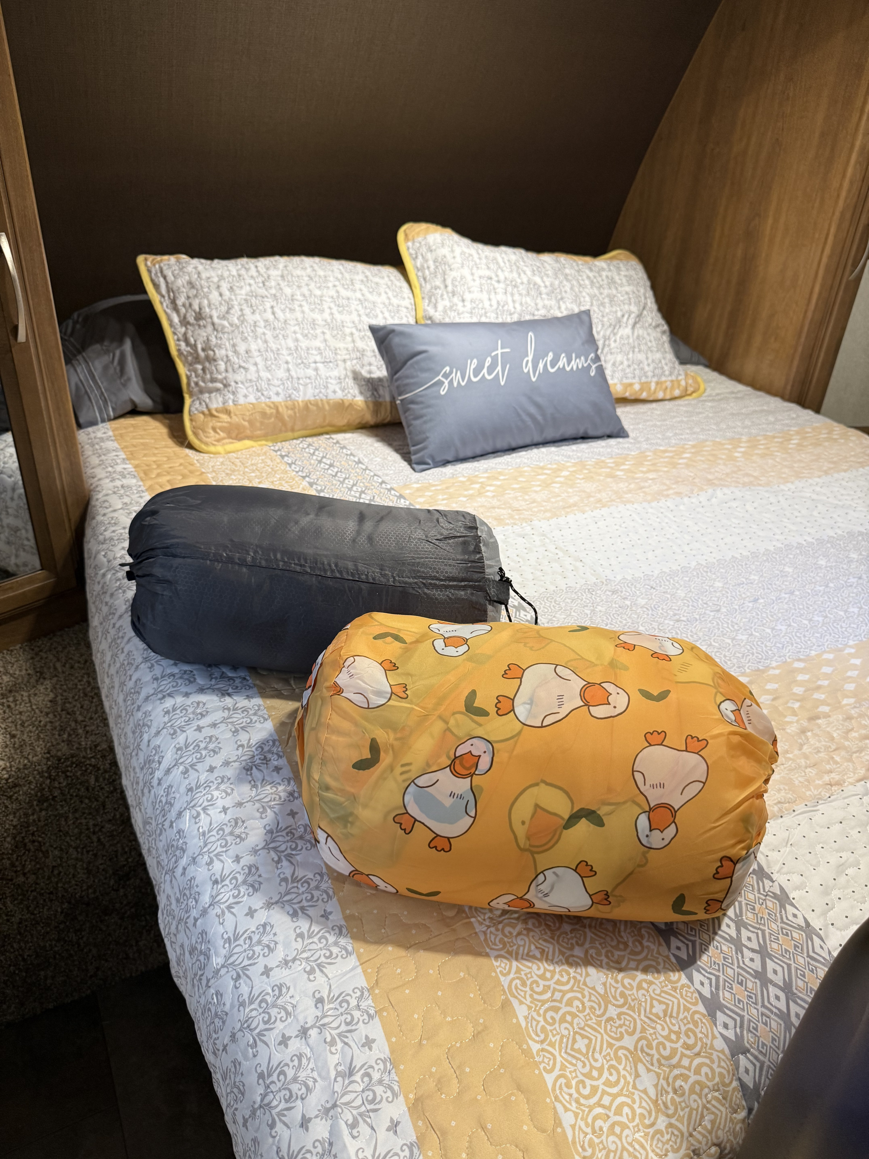 Inside a cozy RV rental: bed with quilt, pillows, and two compact sleeping bags, one with duck patterns.. Coachmen Apex Ultra Lite 2016
