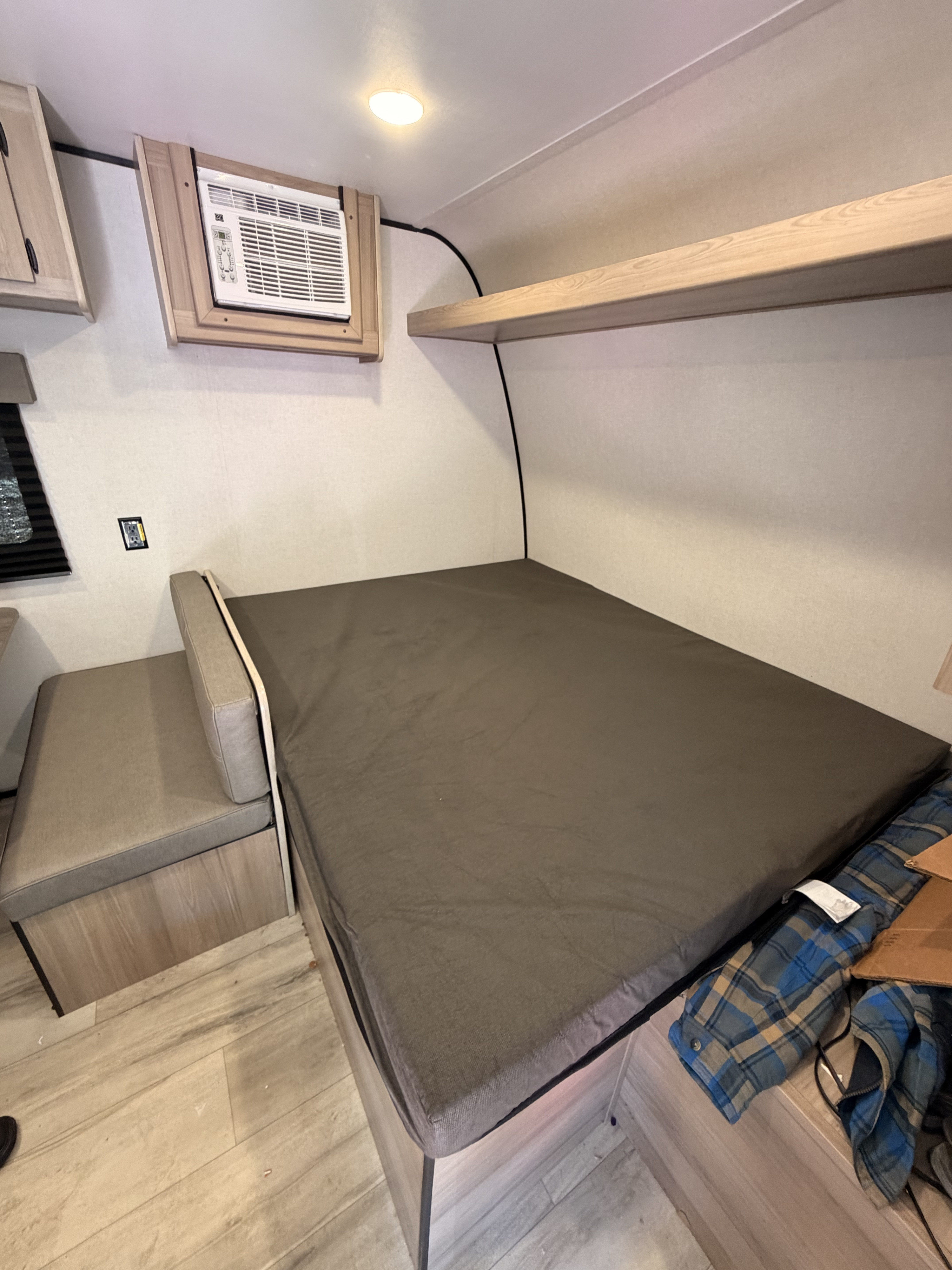 RV rental interior showing a bed, cushioned bench, wall-mounted AC unit, and wooden overhead shelf.. COLEMAN 17B 2025