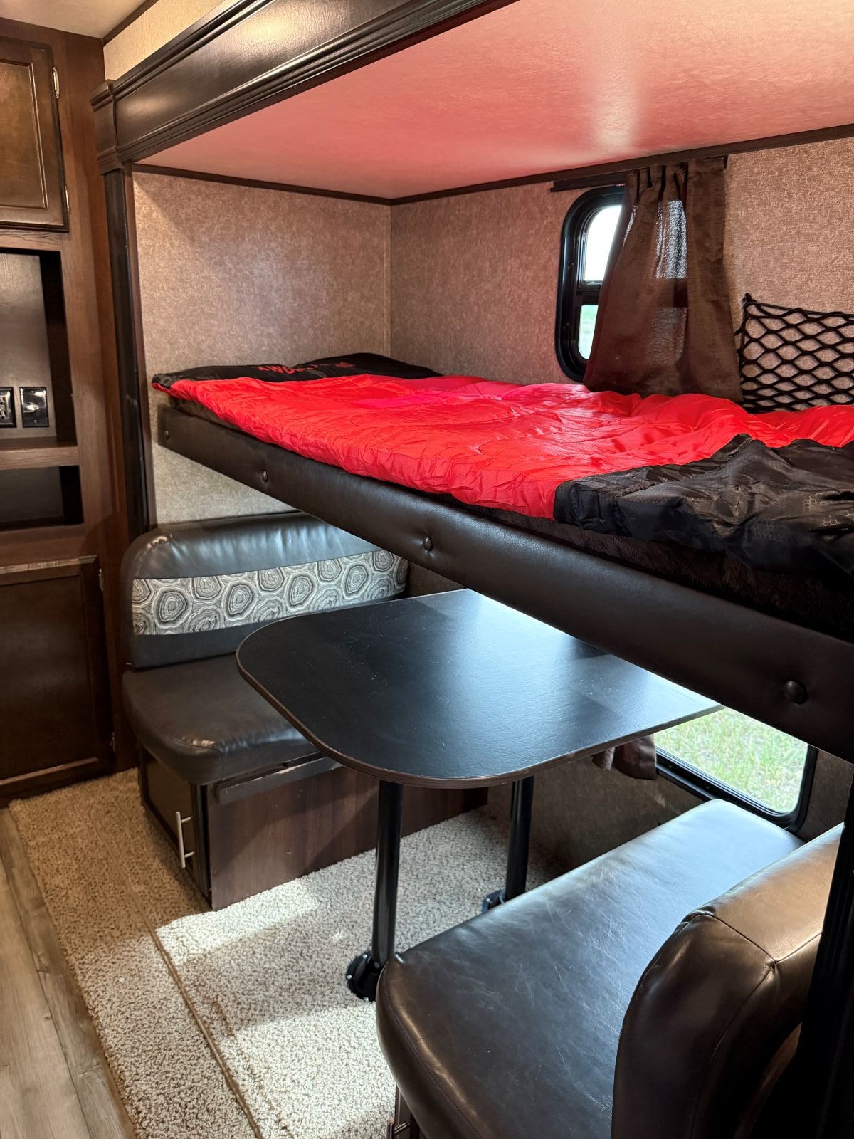 An RV rental interior with a bunk bed (red sleeping bag), a dinette with dark upholstered benches & black table.. Jayco Jay Flight 2019