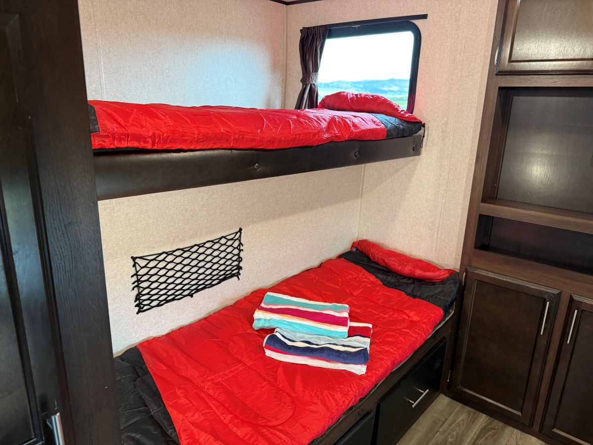 Cozy RV rental bunk beds, with red sleeping bags, scenic window view, and built-in storage. Ideal for family travel.. Jayco Jay Flight 2019
