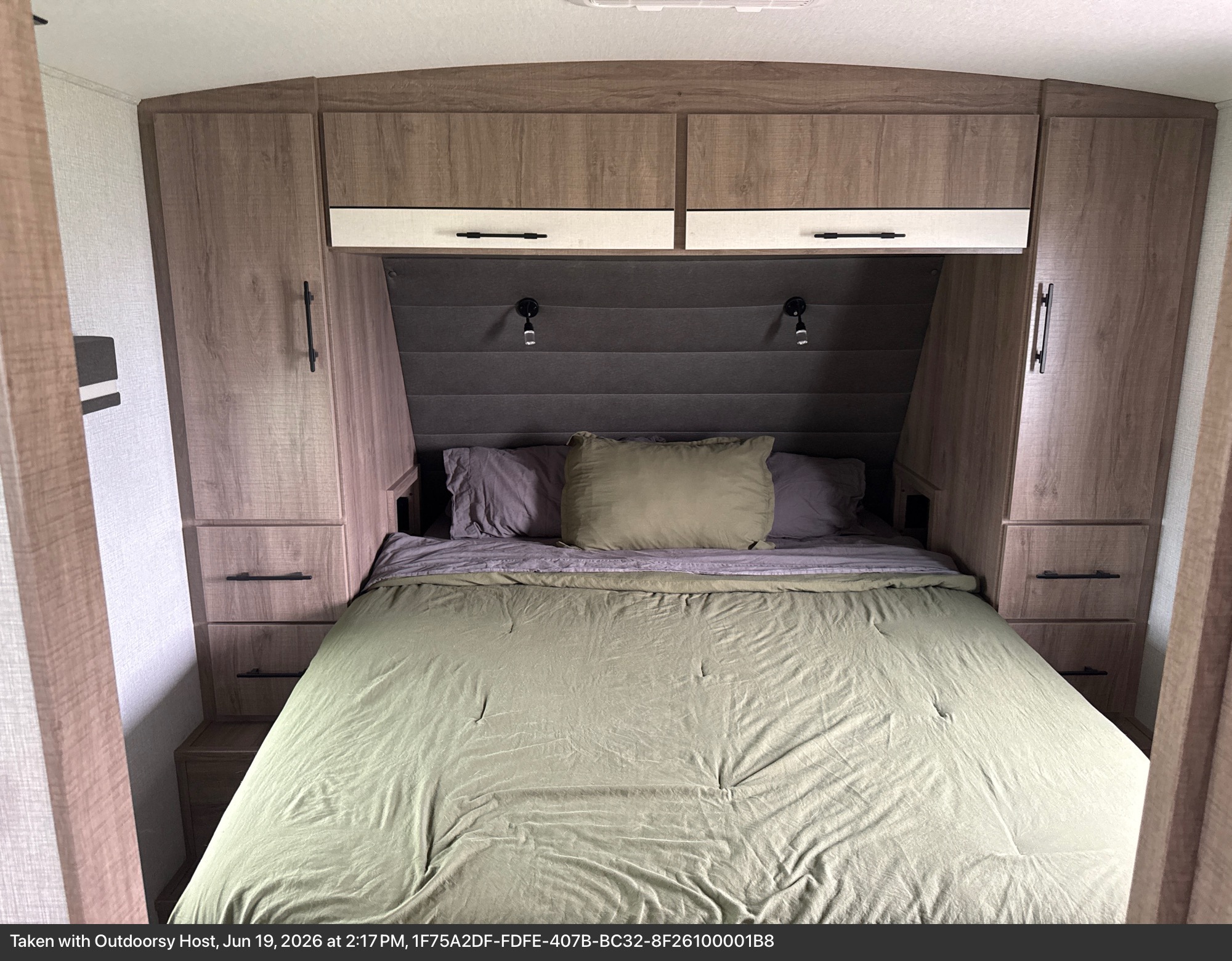 Comfortable RV rental bedroom featuring a bed with green comforter, overhead cabinets, and side storage.. Grand Design Imagine 2024