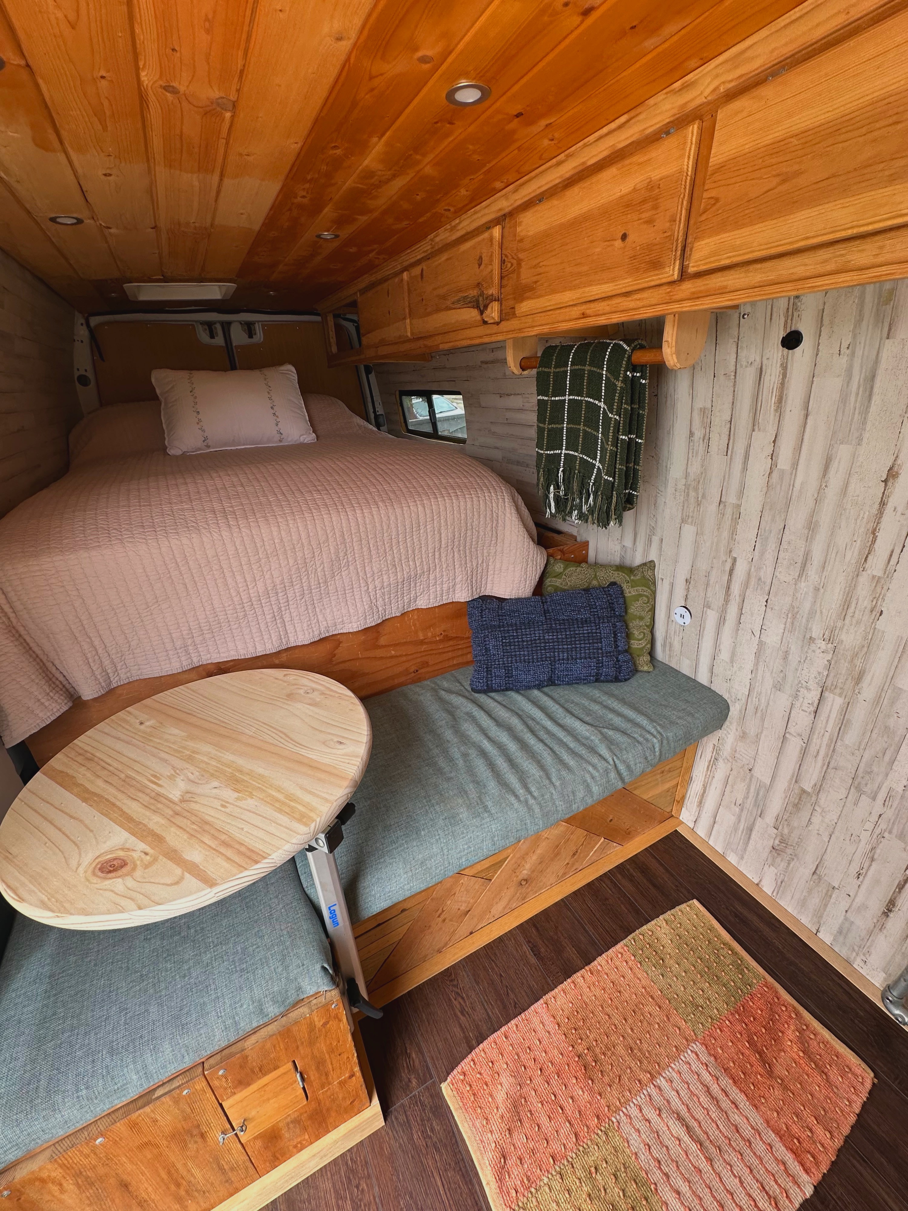 Cozy RV rental interior featuring a comfy bed, convertible dining area, and warm wooden finishes in a rustic van conversion.. Mercedes-Benz Sprinter 316 2008