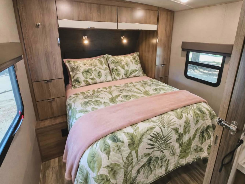 Cozy RV rental bedroom featuring tropical leaf bedding, built-in storage, and ambient lighting for a comfortable journey.. Grand Design Imagine 2021