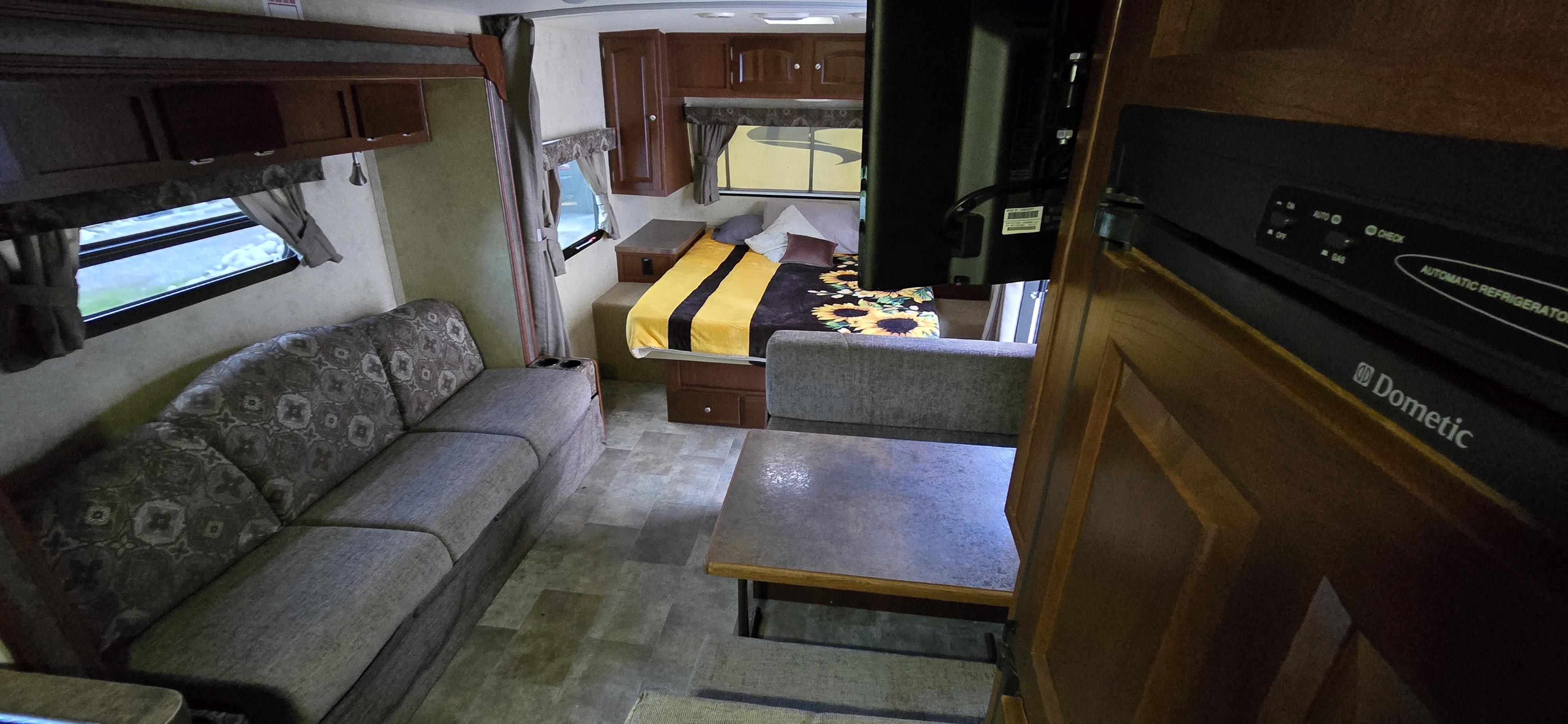Cozy RV rental interior: living area with sofa, bed with sunflower blanket, TV, and Dometic refrigerator.. Forest River Flagstaff Micro Lite 2015
