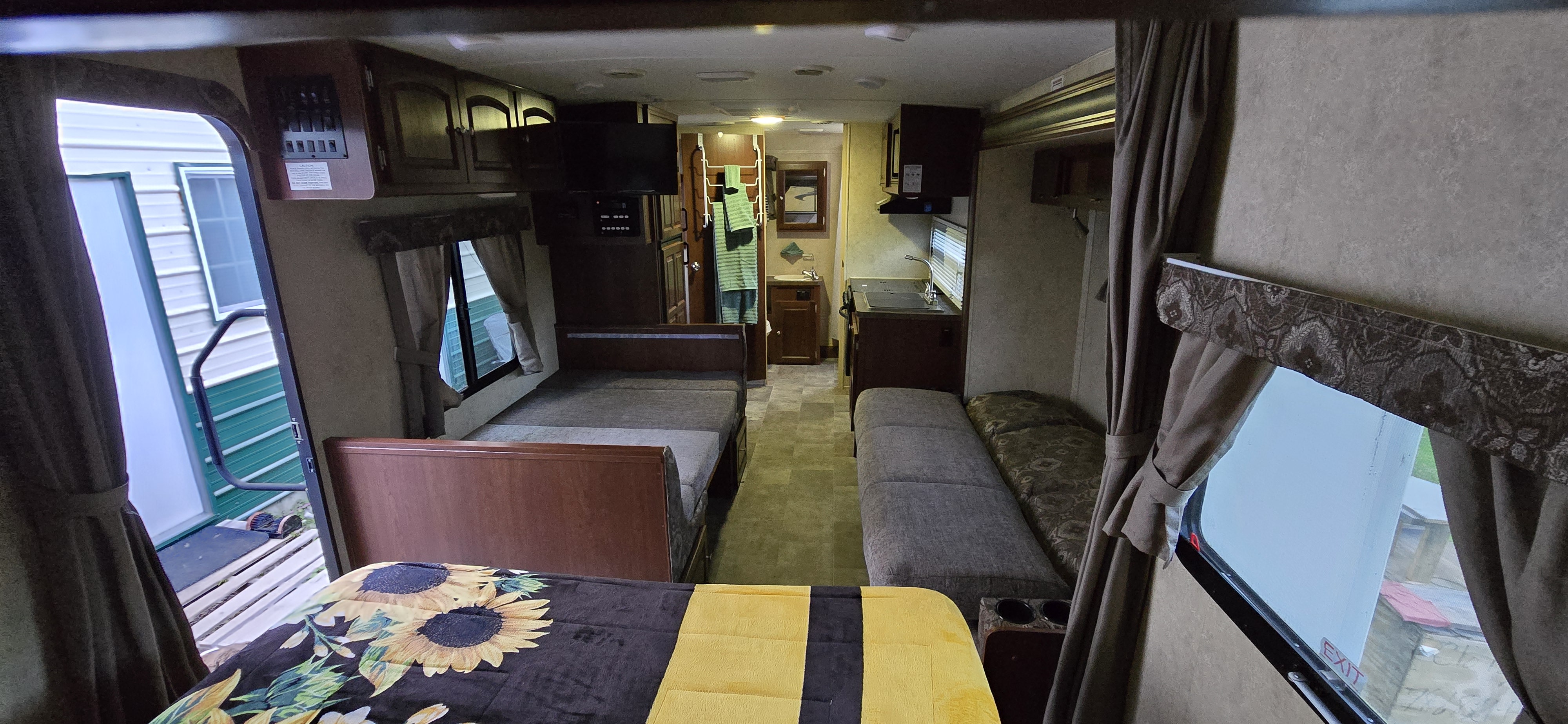 Tour this cozy rv rental interior, featuring beds (one with sunflower print), compact kitchen, and bathroom. Open door view.. Forest River Flagstaff Micro Lite 2015