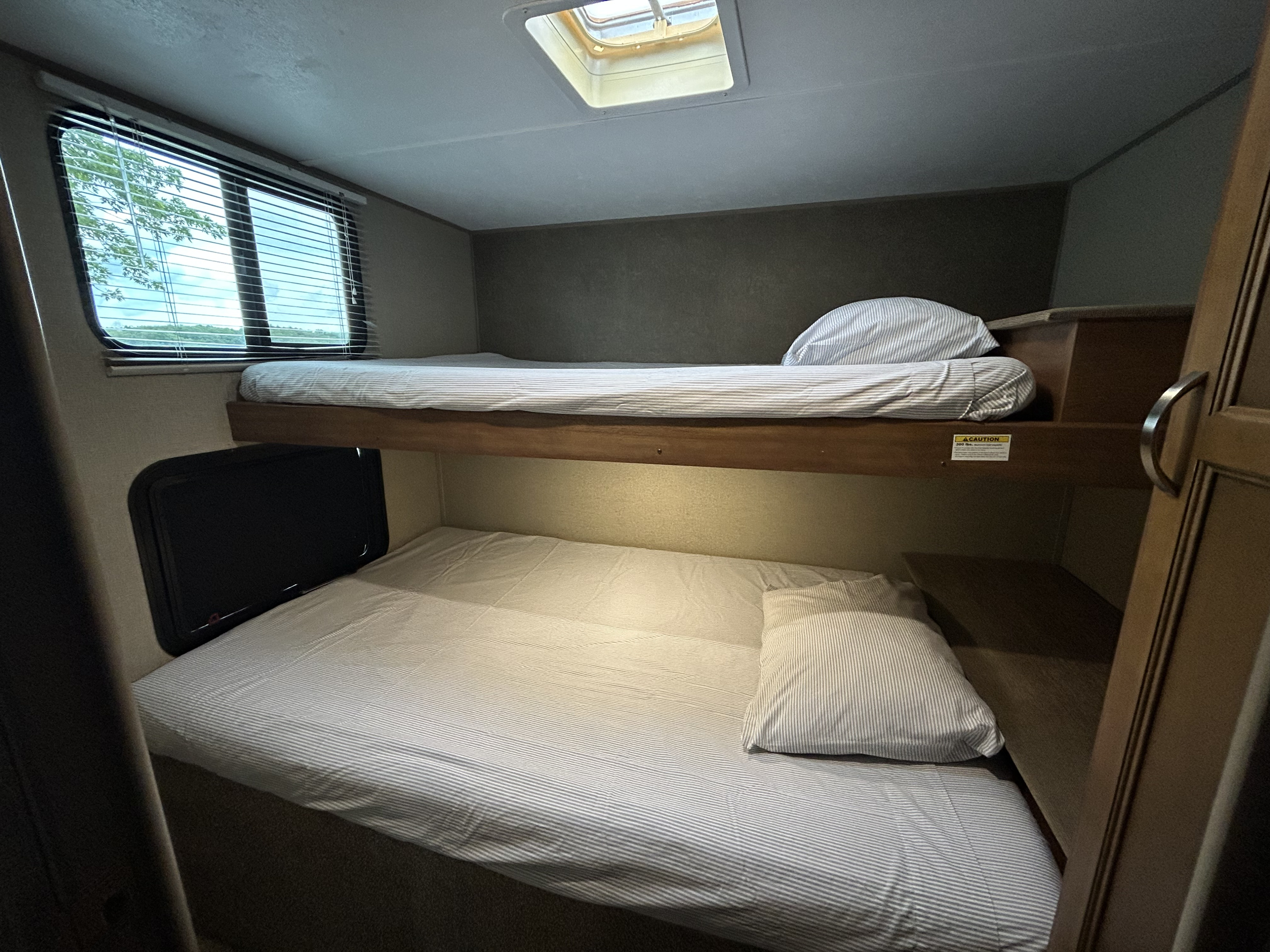 Cozy RV rental bunk beds feature striped bedding, a window with outdoor views, and a ceiling skylight.. Keystone RV Summerland 2018