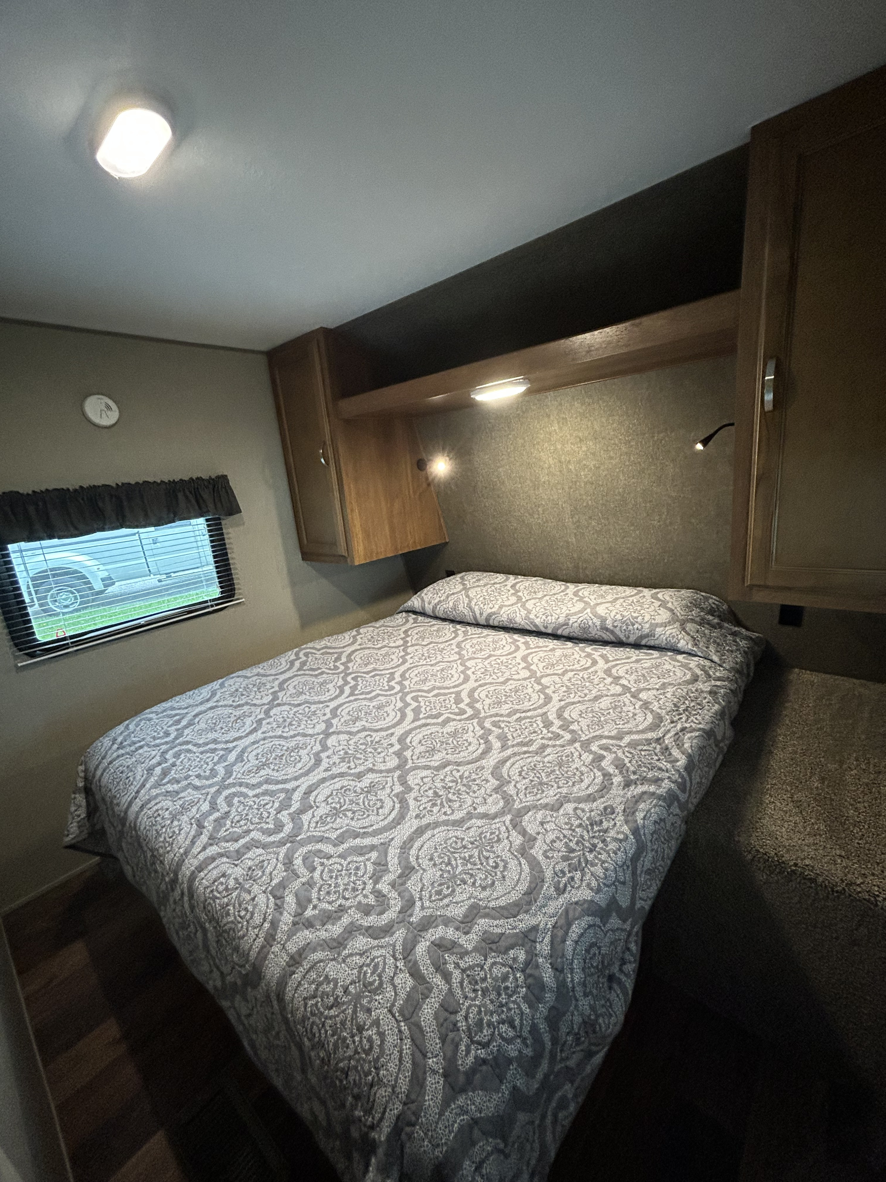 RV rental bedroom featuring a patterned bedspread, window, built-in cabinetry, and ceiling lighting. Enjoy comfortable travels!. Keystone RV Summerland 2018