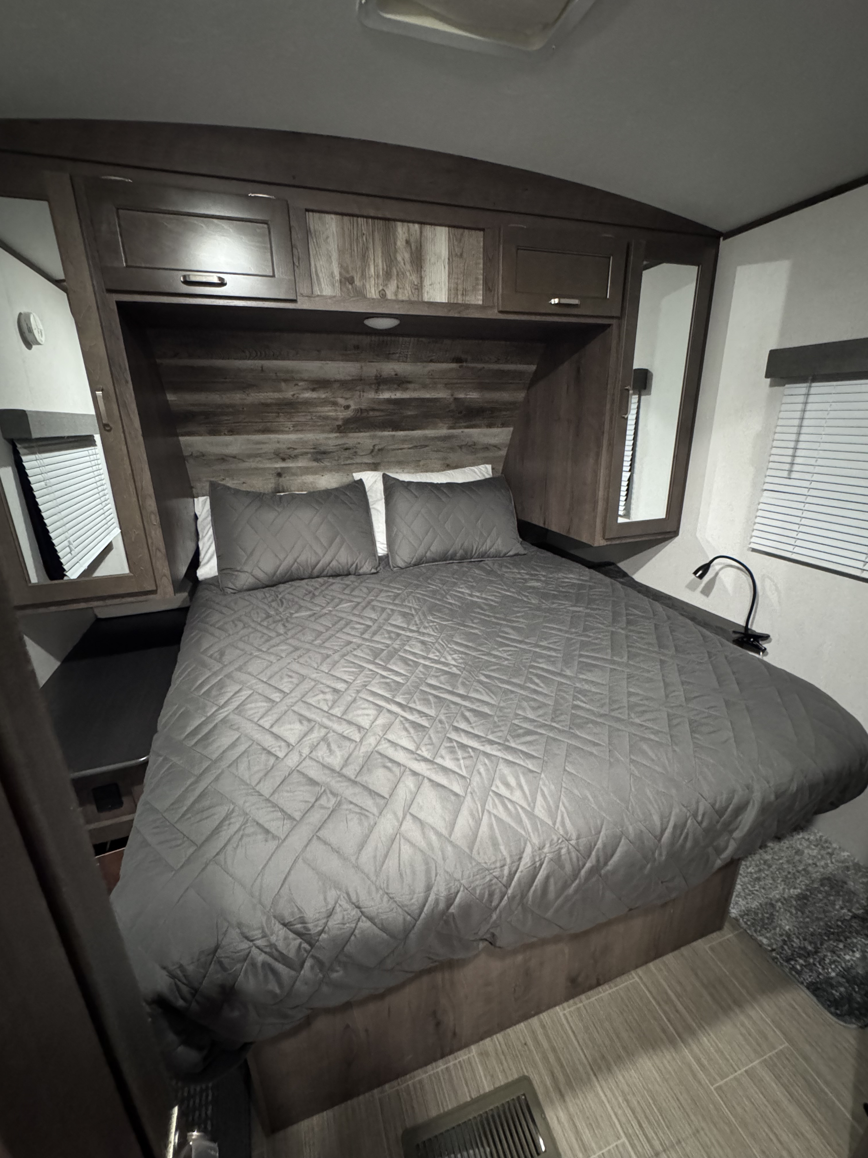 RV rental bedroom showing a well-made bed, rustic wooden cabinets, and mirrored wardrobes for a cozy stay.. Keystone RV Passport Grand Touring 2021