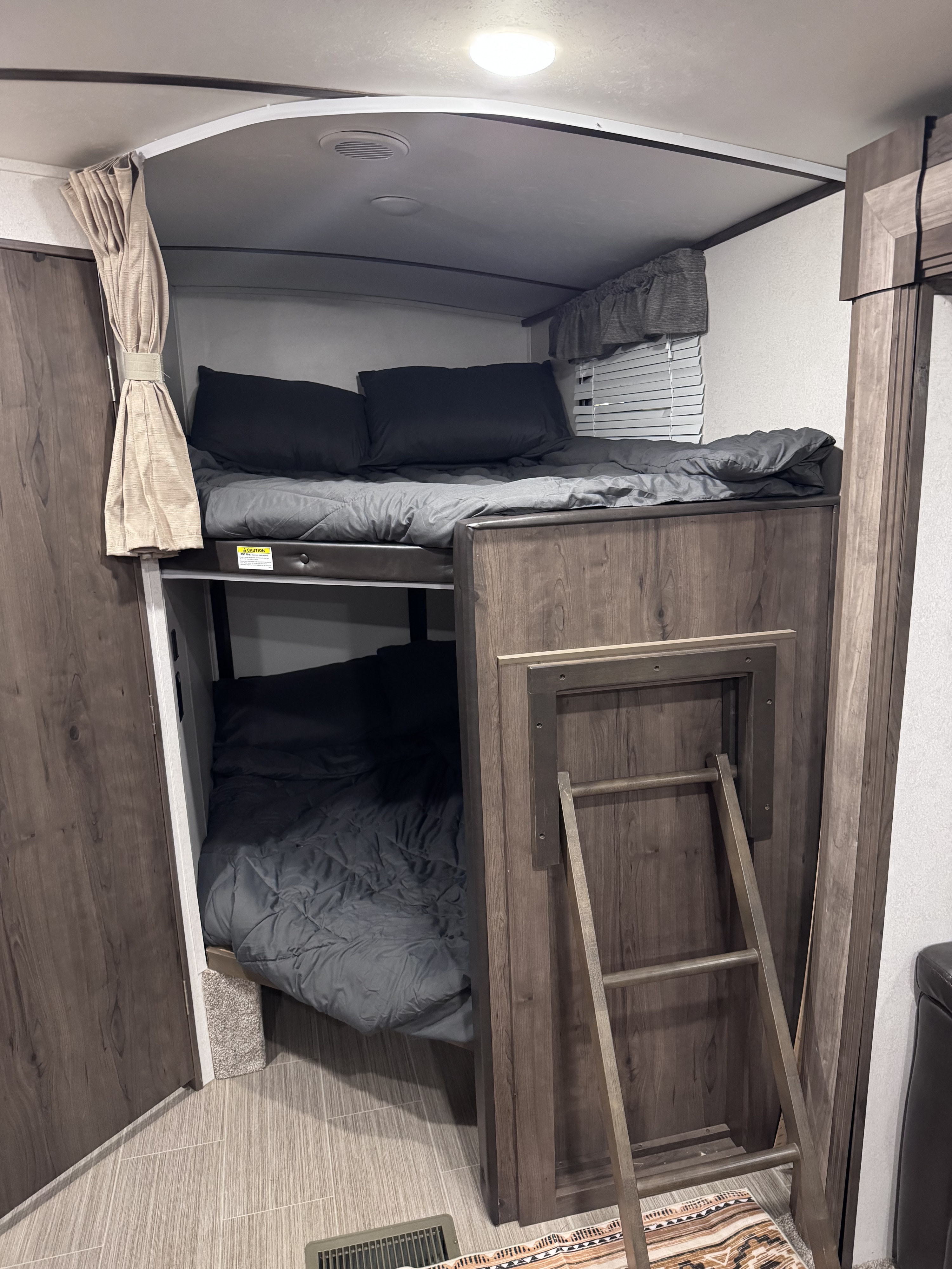 Inside an RV rental, two bunk beds with dark gray bedding and a wooden ladder for access.. Keystone RV Passport Grand Touring 2021