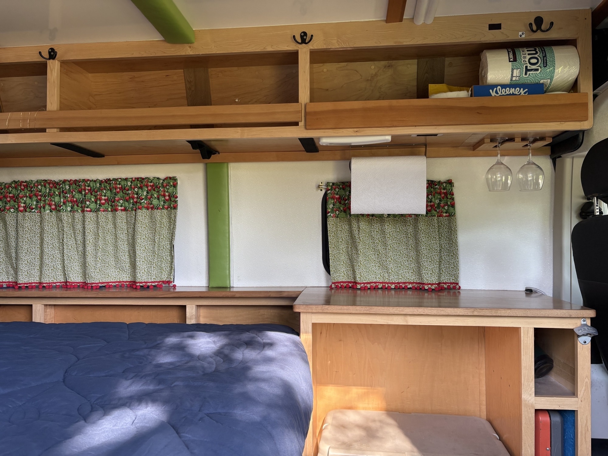 Cozy RV rental interior: wooden shelves, bed with blue comforter, practical storage, and charming strawberry curtains create a functional space.. Dodge Ram 1500 2016