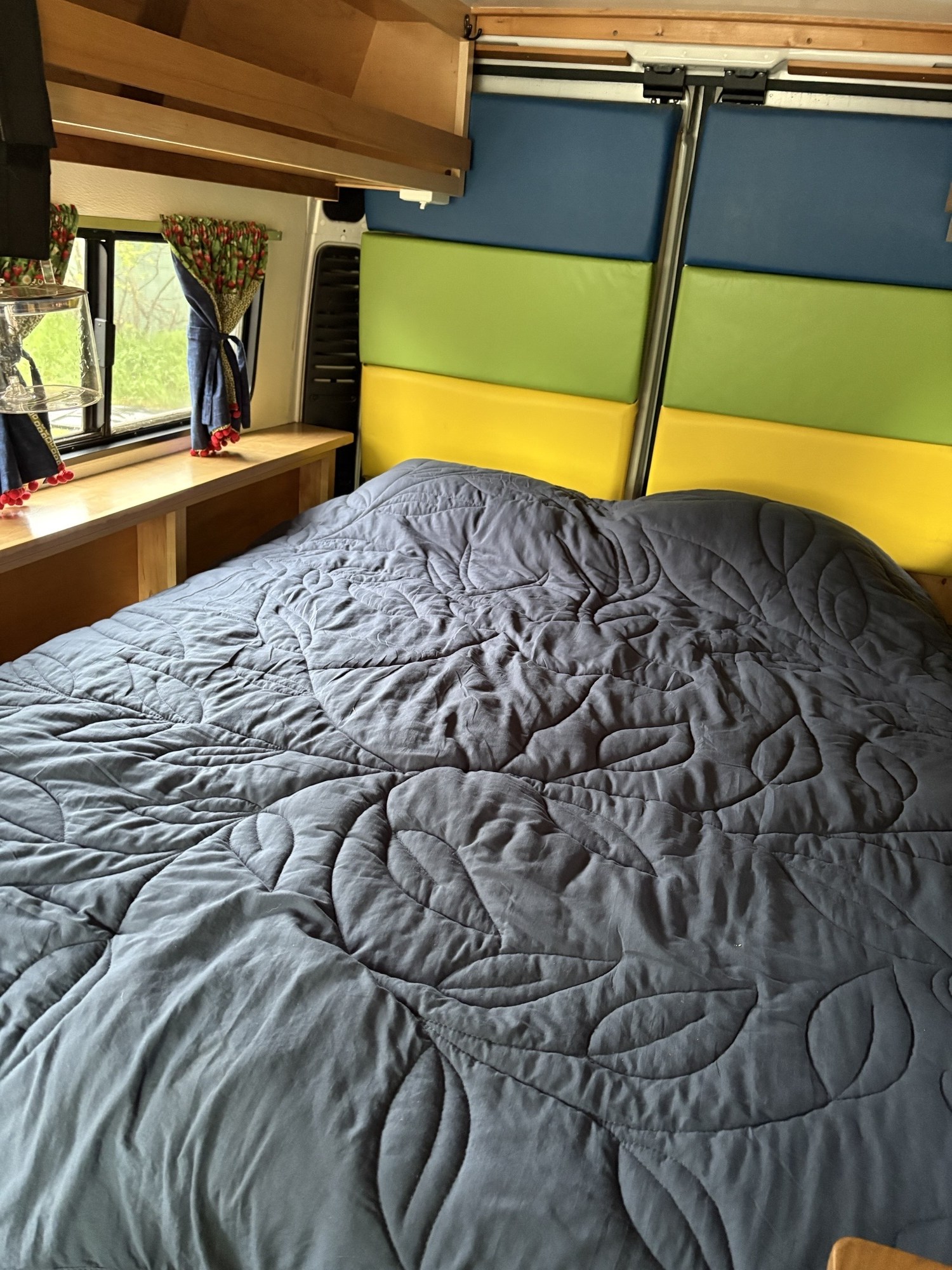 Cozy rv rental interior featuring a bed with a quilted comforter, colorful padded walls, and patterned window curtains.. Dodge Ram 1500 2016