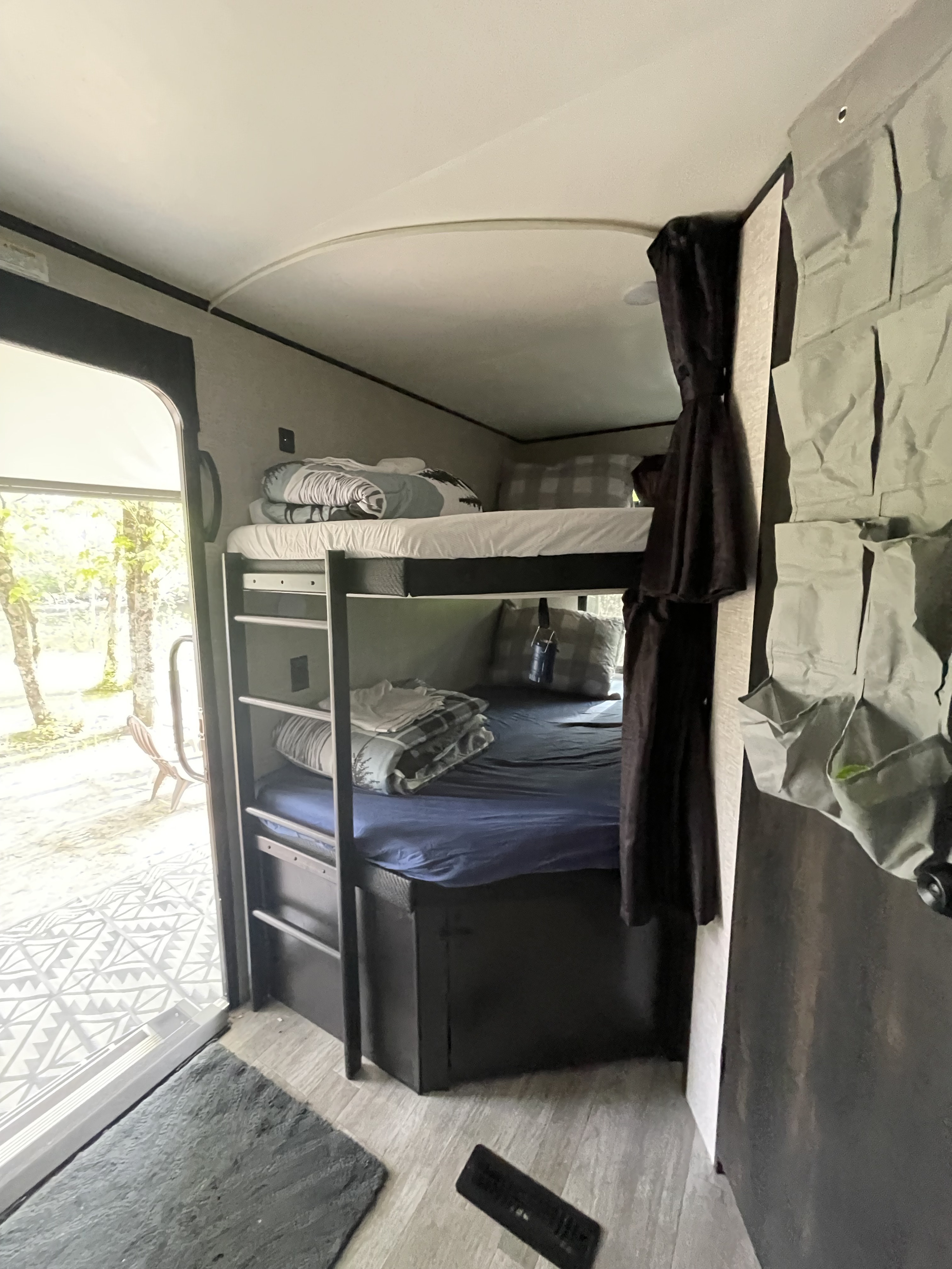 This RV rental features cozy bunk beds with blue and white bedding, an open door to nature, and wall storage pockets.. Jayco Jay Flight 2022
