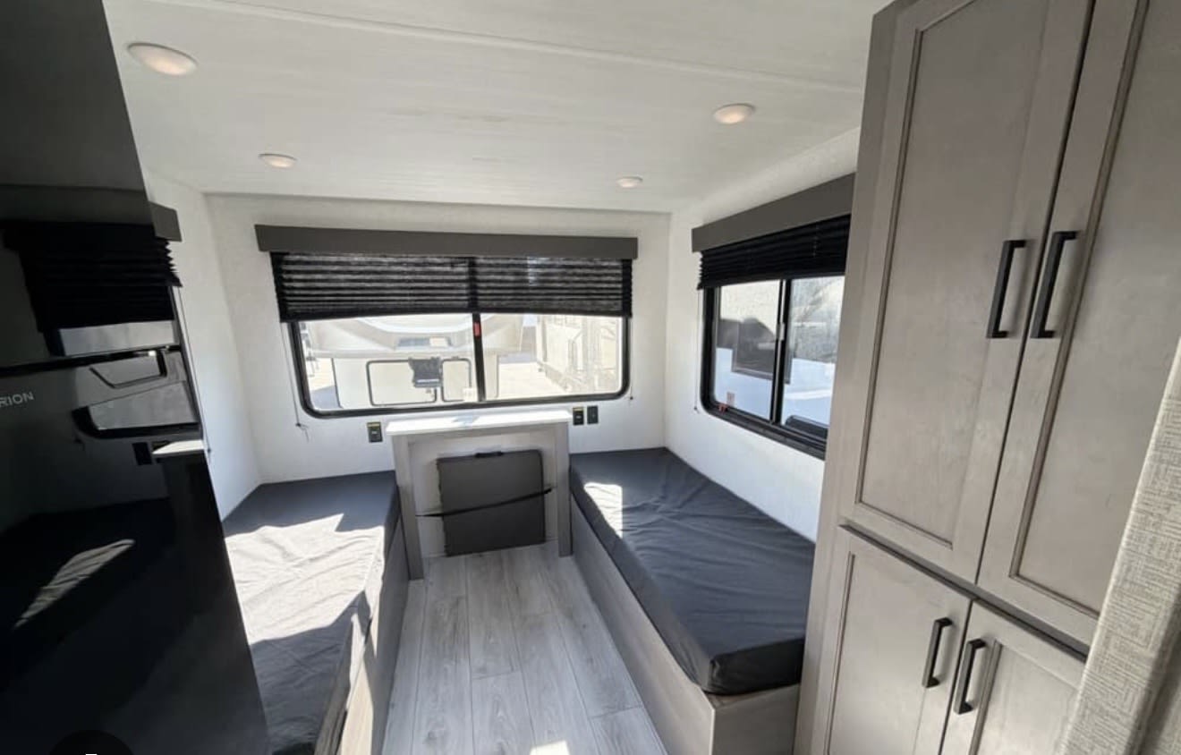 This rv rental offers a compact sleeping area with two beds, windows, built-in storage, and bright interior lighting.. Keystone RV Hideout Sport 2025