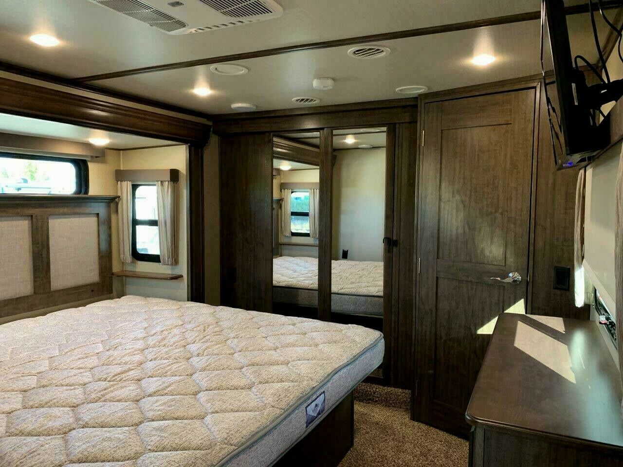 Spacious RV rental bedroom featuring a comfortable bed, mirrored wardrobe, and windows for your trips.. Grand Design Solitude 2018