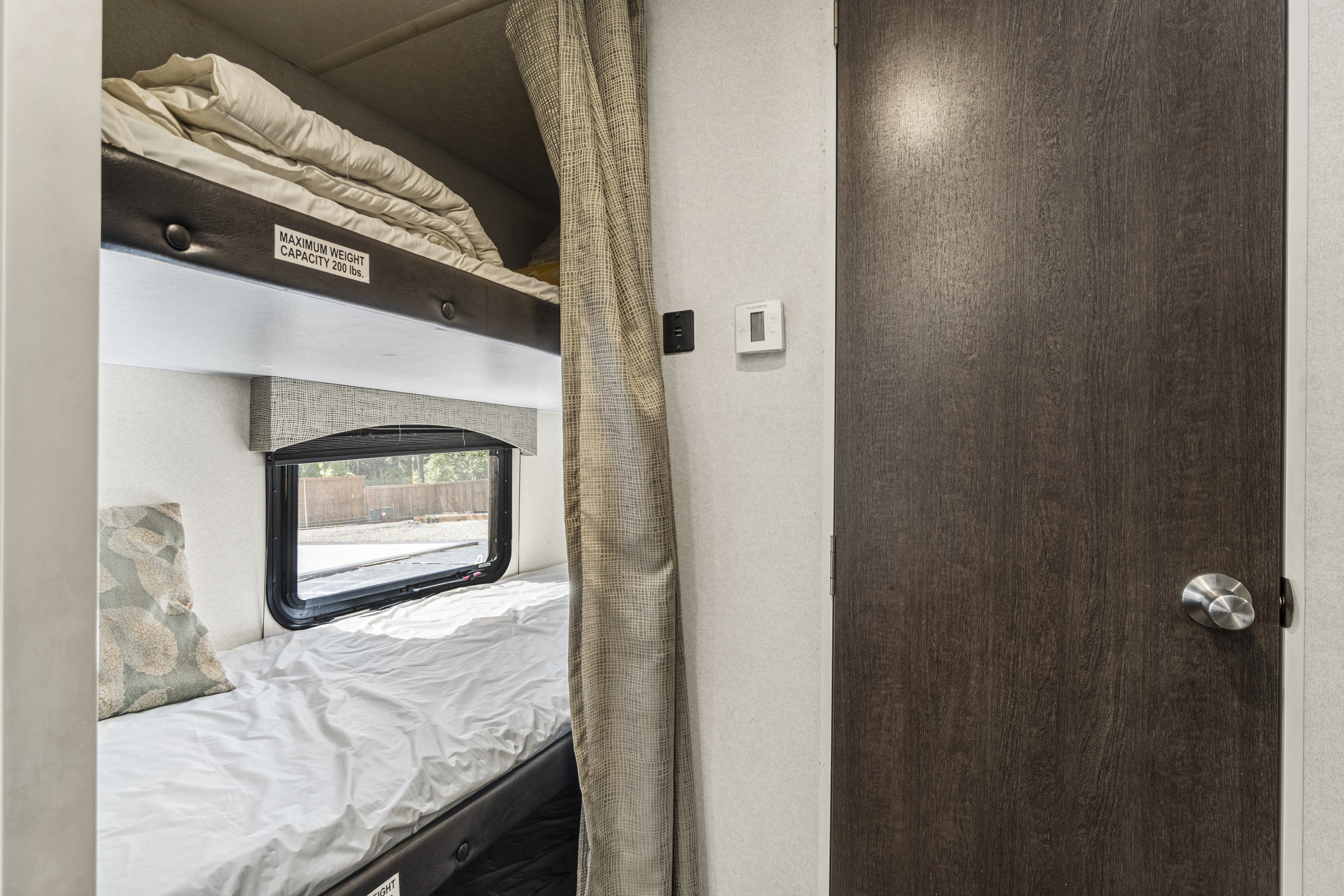 This RV rental interior features bunk beds with a window, privacy curtain, door, and a Dometic thermostat with USB charging.. Forest River Evo T2550 2019