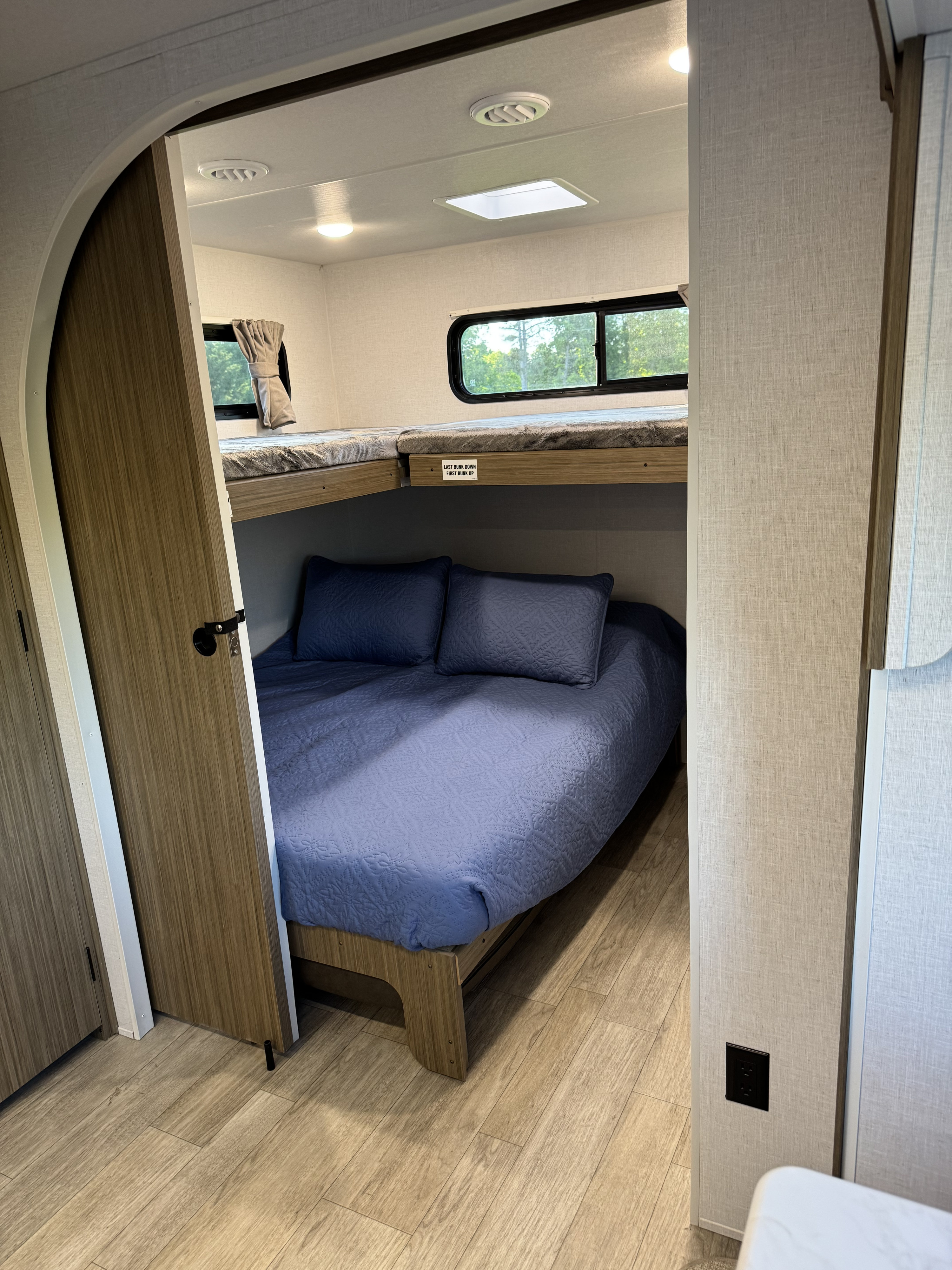 Cozy RV rental sleeping area with a full-size bed below an upper bunk, visible through an open archway and doorway.. Forest River Wildwood FSX Platinum 2026