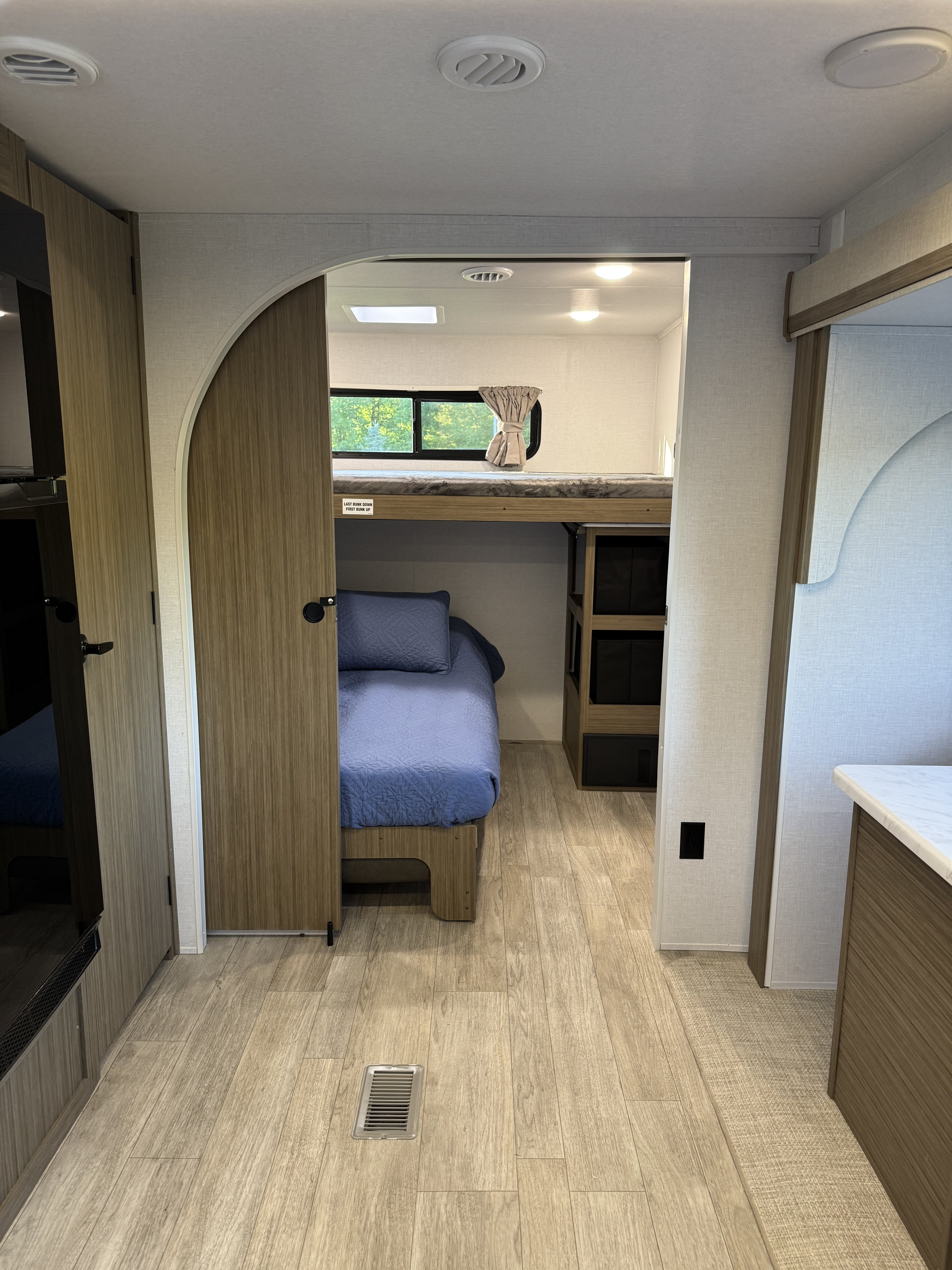 Modern rv rental bunk room with blue bedding, wood accents, and bright natural light through the window.. Forest River Wildwood FSX Platinum 2026