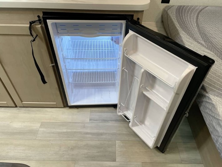 Open, empty mini-fridge in an RV rental, showing interior shelves and door storage. Ready for your groceries!. Jayco Heartland Prowler Lynx 2026
