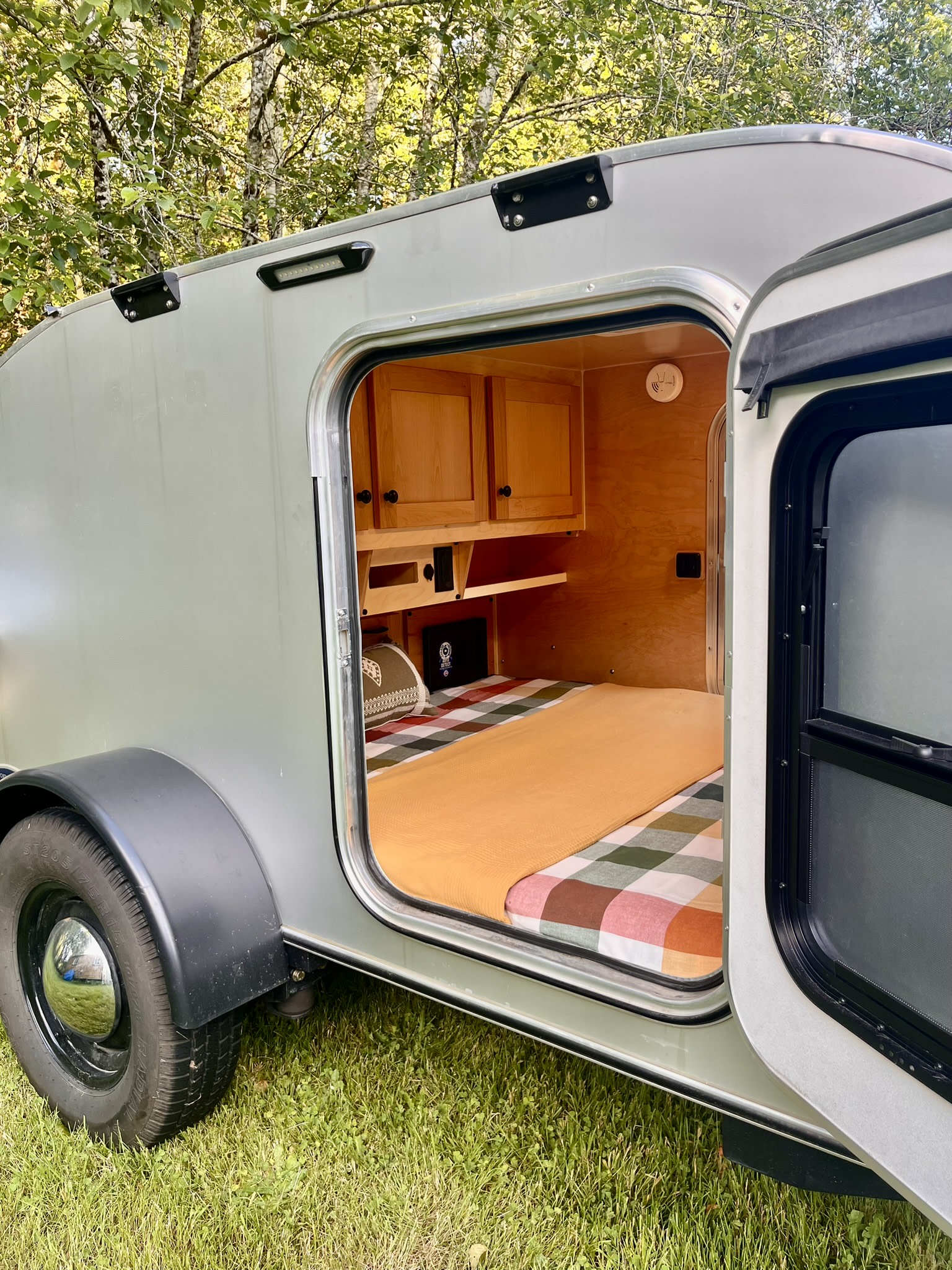 Explore this cozy teardrop camper interior, perfect for an RV rental. Features a comfy bed, wooden cabinets, and ready for outdoor adventures.. Aero Steel 2022