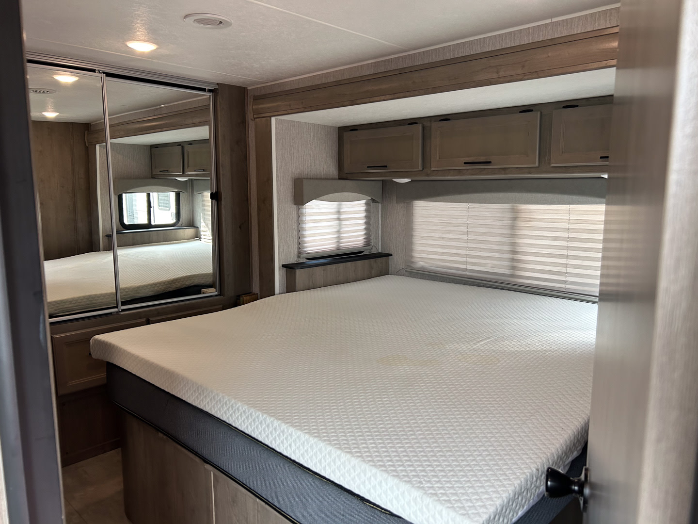 Experience comfort in this clean RV rental bedroom. Features a large bed, overhead cabinets, and mirrored closet. Ideal for travel.. Coachmen Freelander 2021