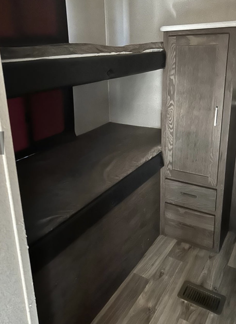 This **rv rental** offers a sleeping area with two dark bunk beds, next to a wooden cabinet with a door and two drawers.. Forest River Salem Hemisphere Lite 2019