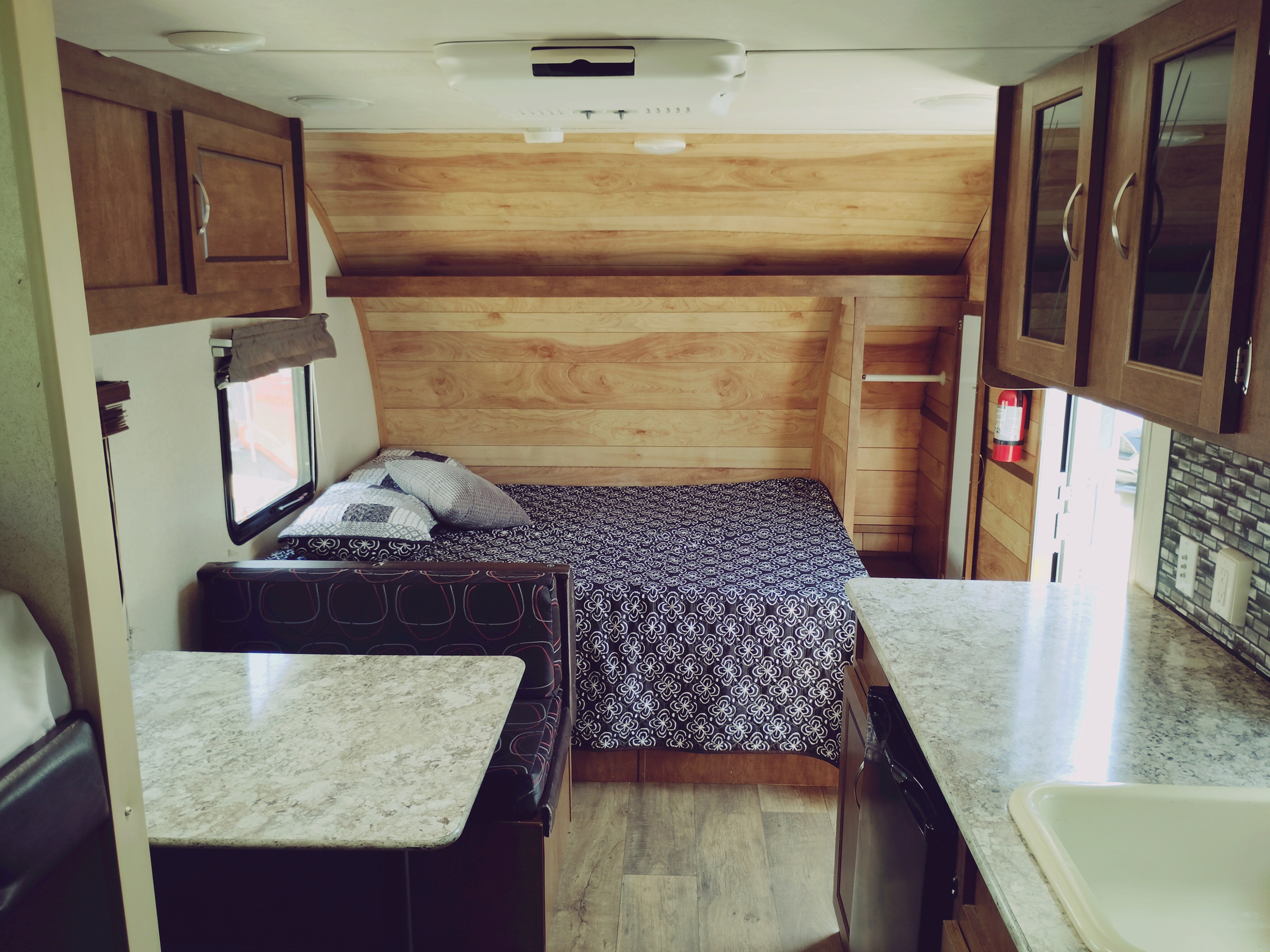 Cozy RV rental interior featuring a bed with patterned bedding, a dinette, and a kitchen counter with a sink. Ideal travel trailer.. Forest River Salem FSX 2017