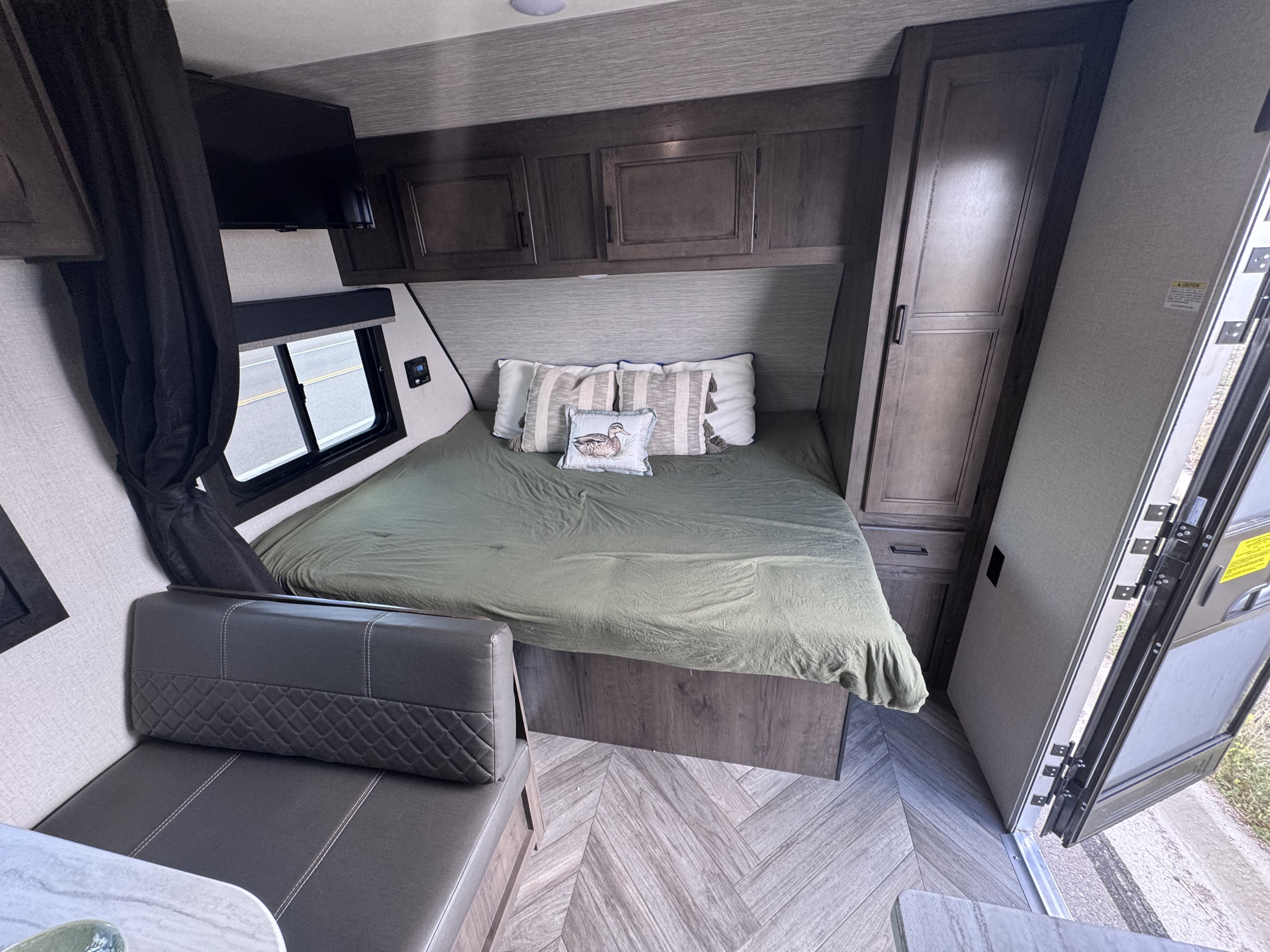 RV rental interior shows a bedroom with a green bed, decorative pillows, overhead cabinets, TV, window, and seating area.. Highland Ridge RV Olympia Sport 2022